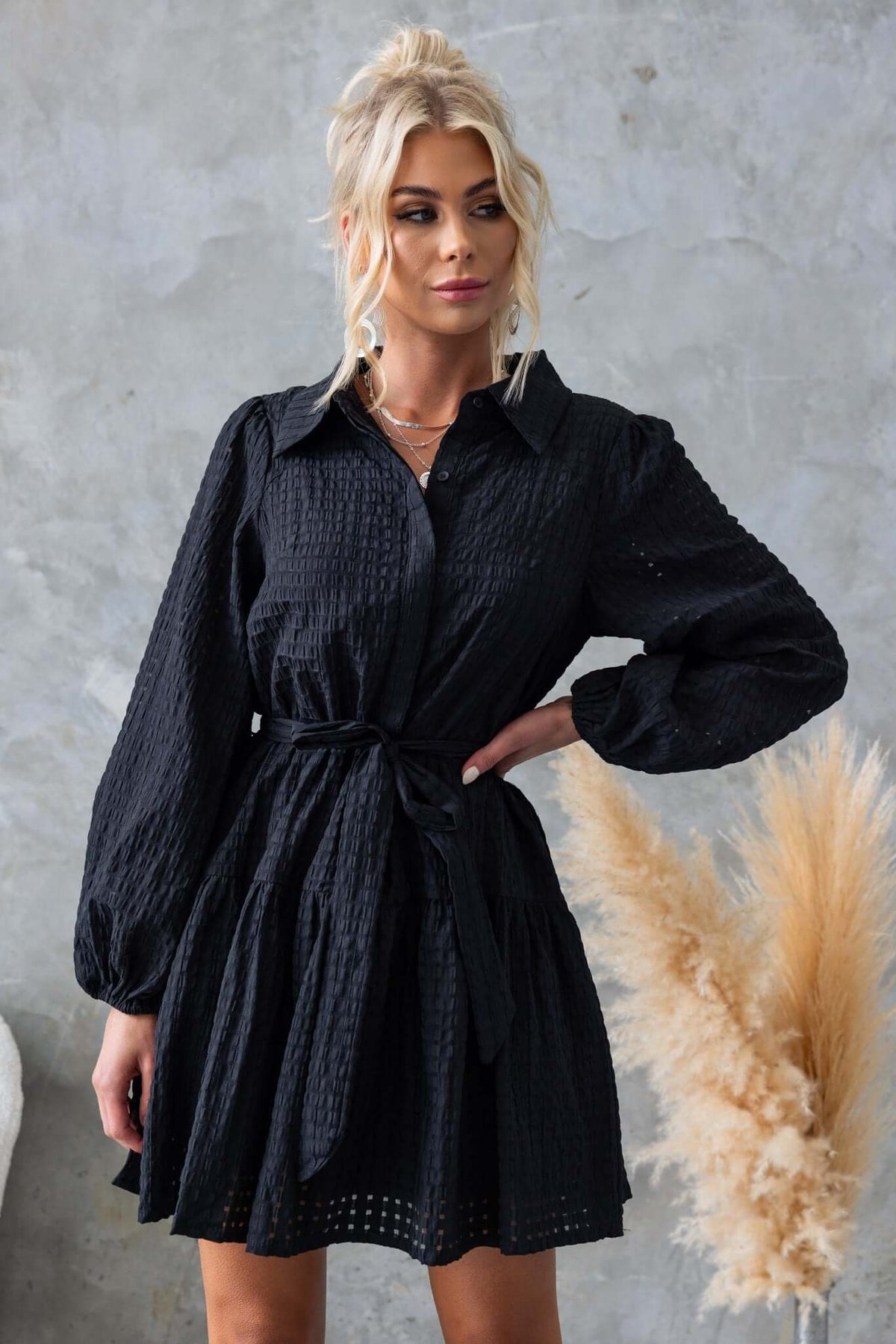 Cottee Dress in black featuring a button-up front, elastic sleeves, removable tie, and pockets, styled with a relaxed fit.