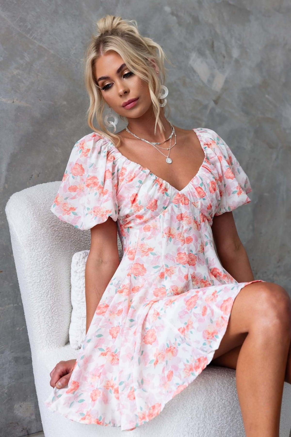 Model wearing a floral Feel Good dress with puffed sleeves and a low-cut back, styled with layered necklaces.