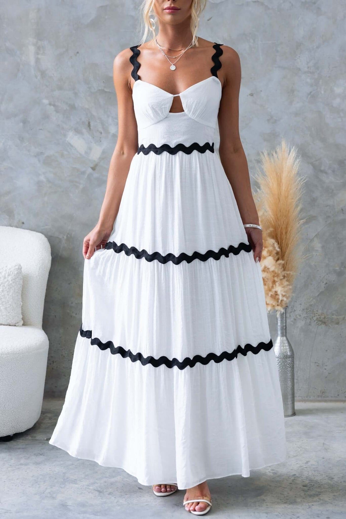 Stylish Qaia Maxi Dress in white with black scalloped straps and cut-out bust, perfect for summer occasions.