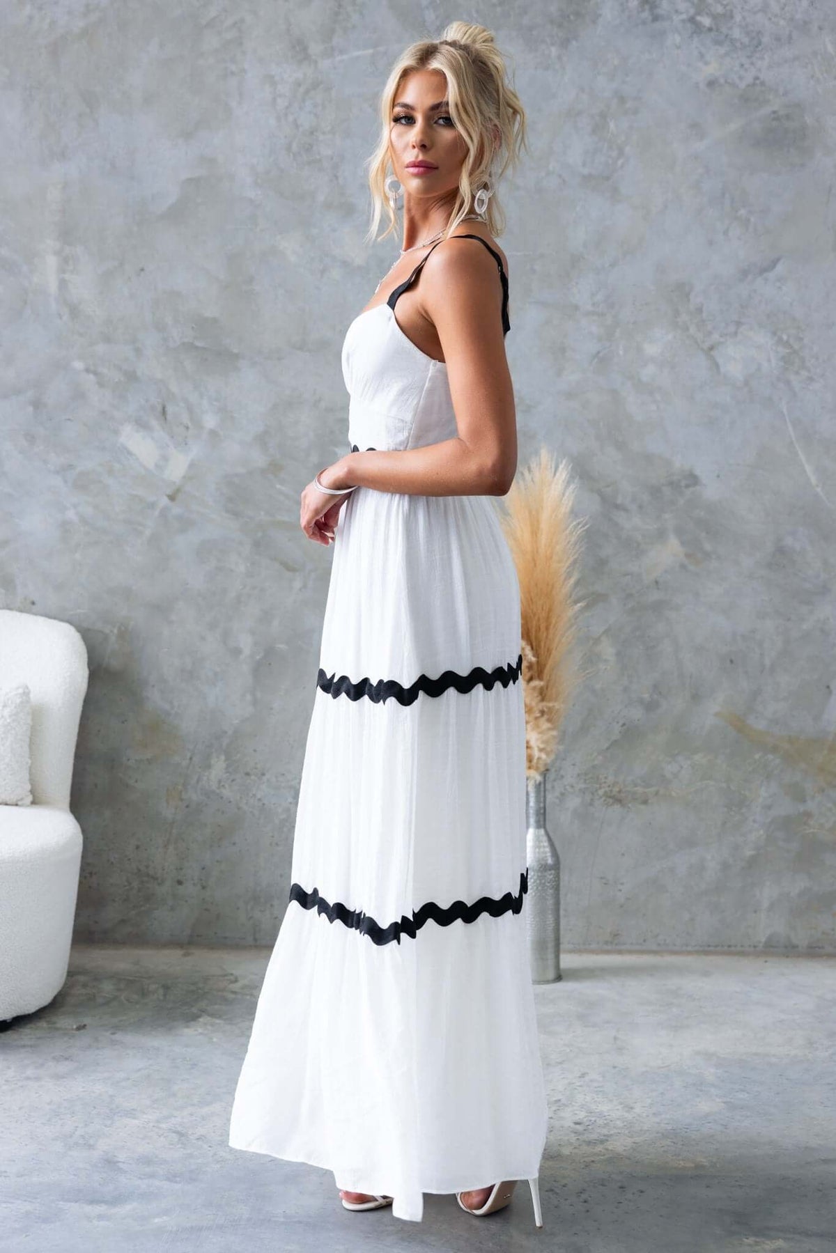 Woman wearing Qaia Maxi Dress, featuring adjustable straps and black accents, styled in a modern setting.