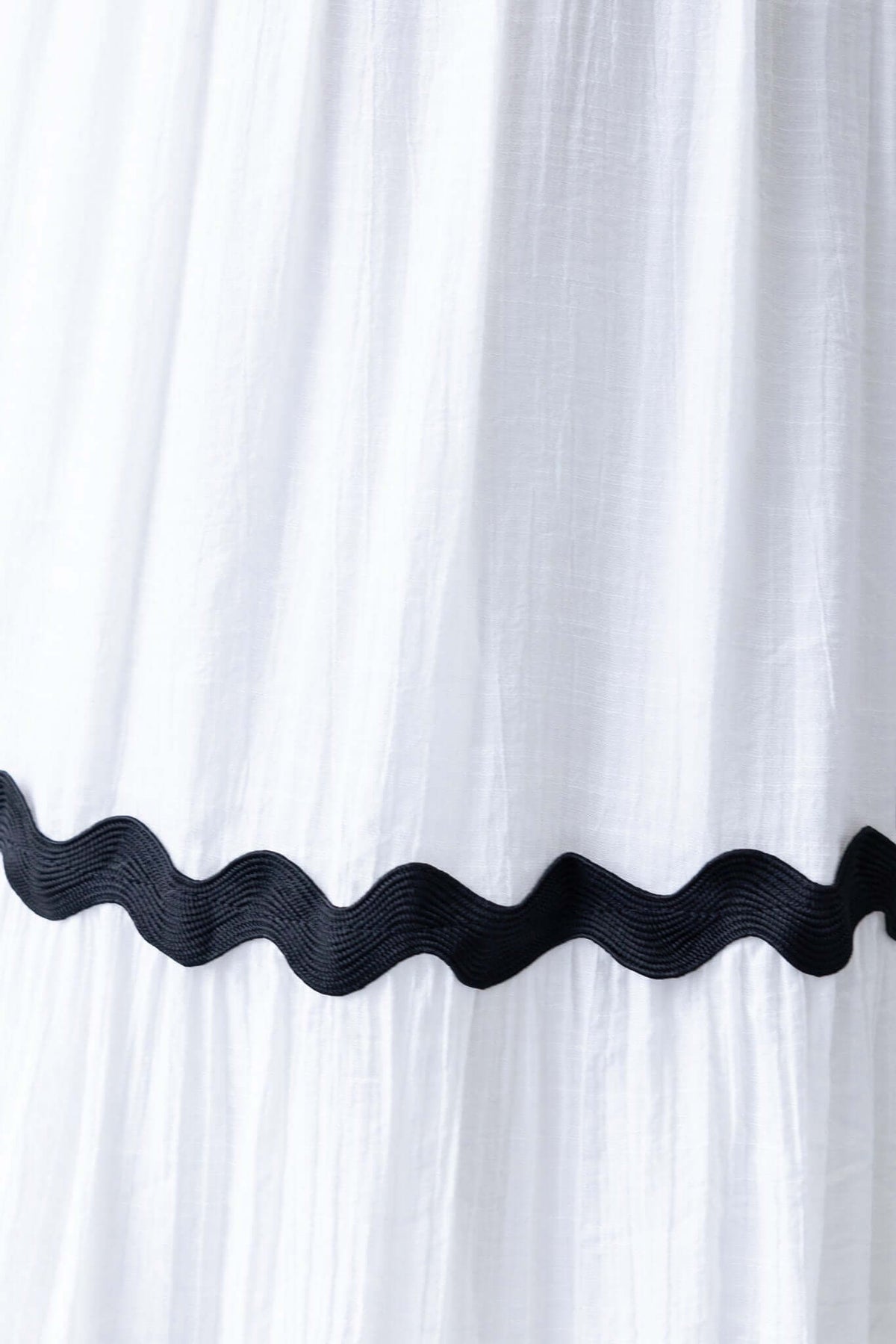 Close-up of a white maxi dress skirt featuring a black wavy trim, showcasing texture and design details.