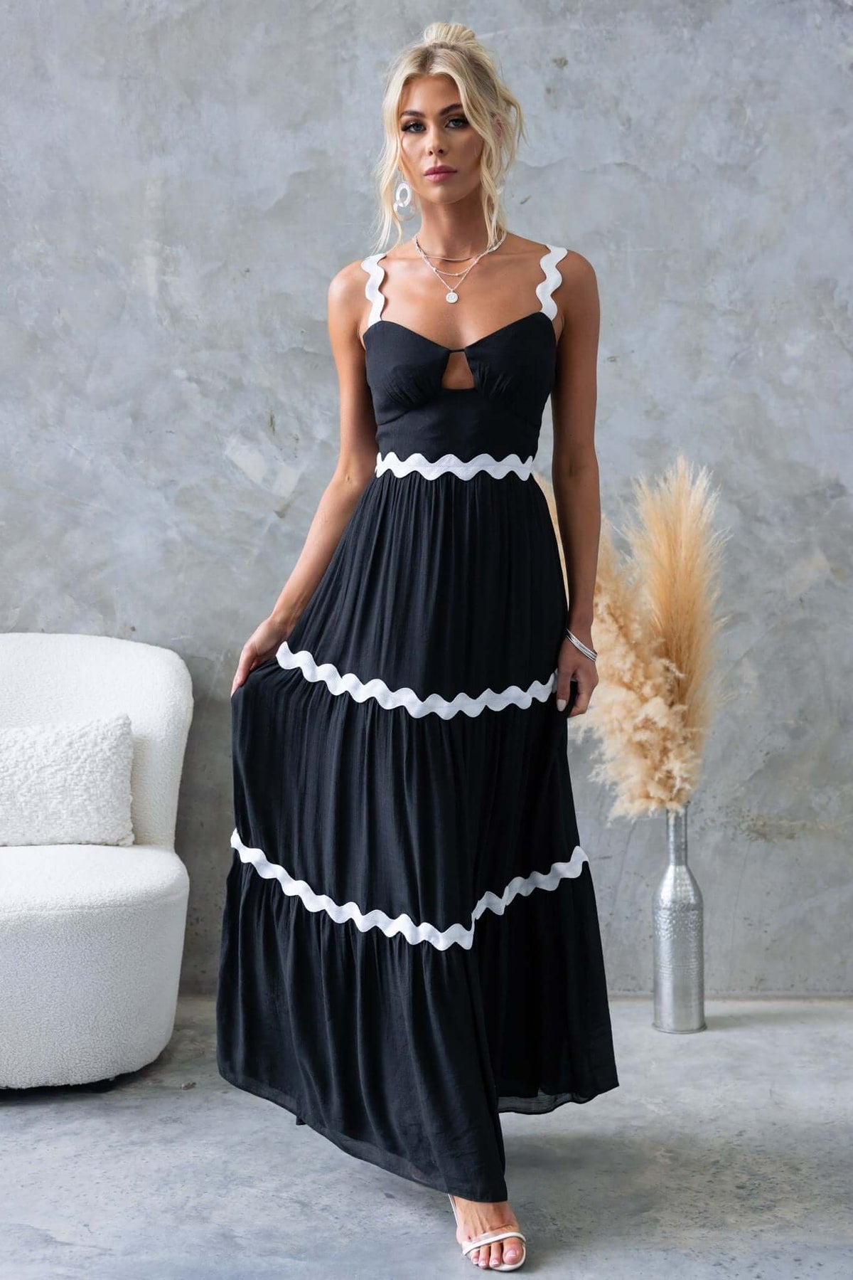Elegant black maxi dress with adjustable straps and cut-out detail, featuring contrasting white ruffles.