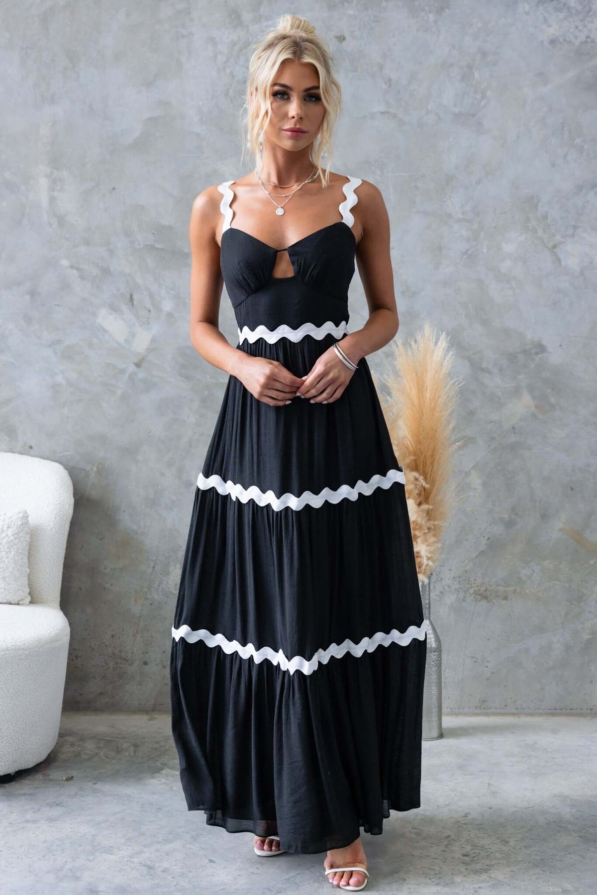 Black maxi dress with adjustable straps and cut-out bust detail, styled with white scalloped trim.