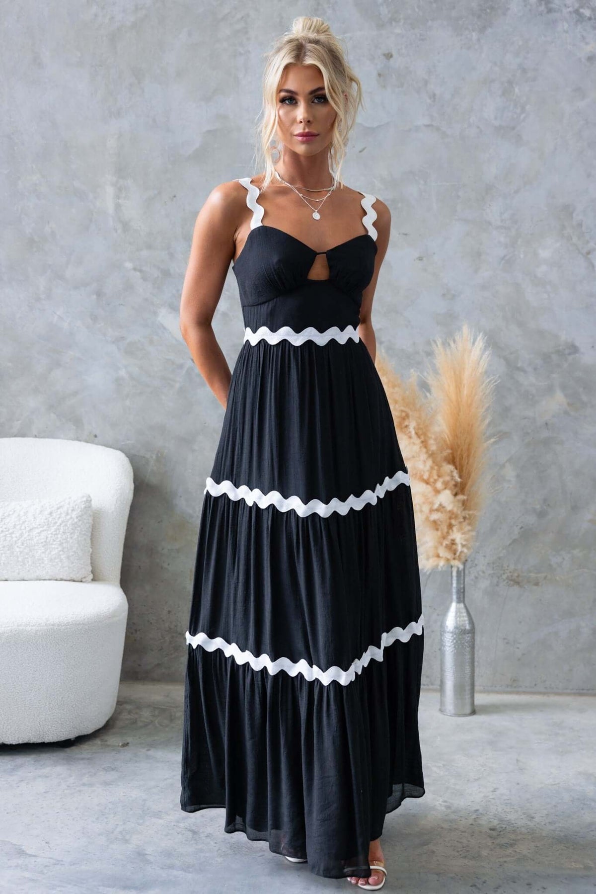 Model showcasing the Qaia Black Maxi Dress with adjustable straps and cut-out bust detail in a stylish setting.