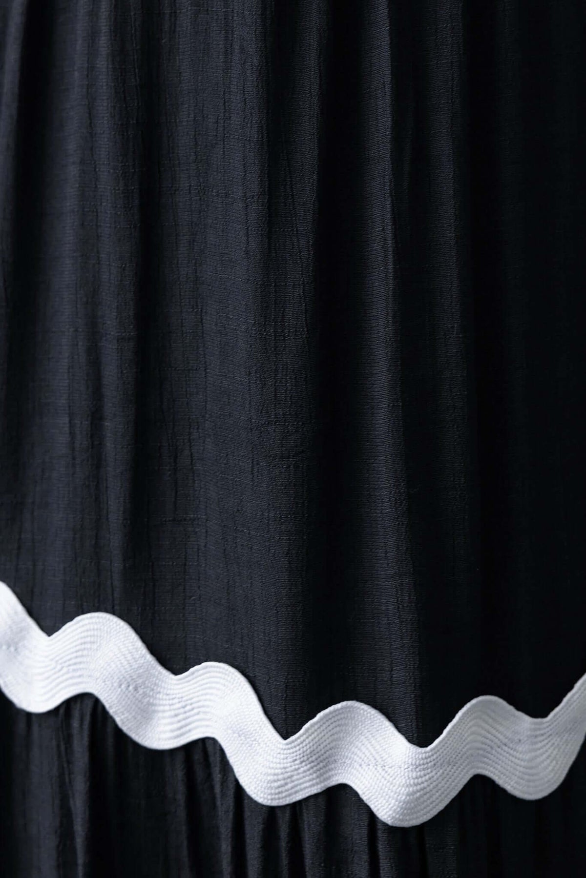 Close-up of black fabric with a white scalloped trim detail on the Qaia Maxi Dress.