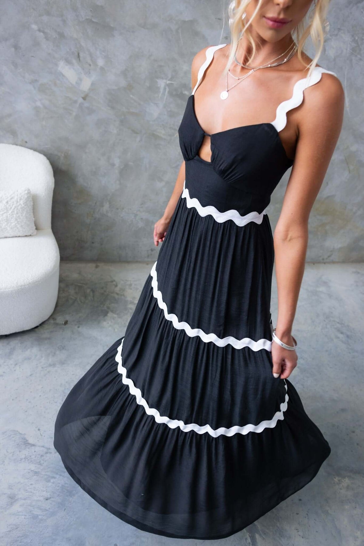 Black Qaia Maxi Dress with adjustable straps and cut-out design, featuring white scalloped trim.
