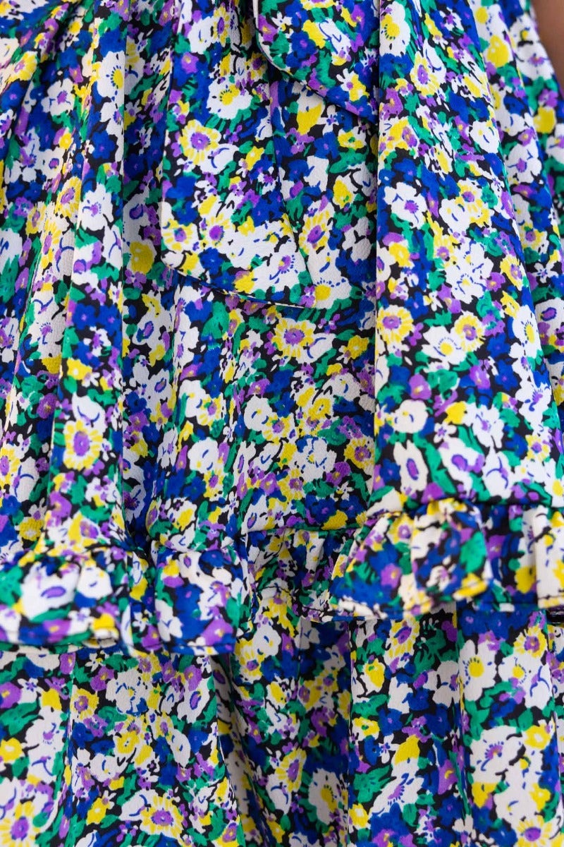 Close-up of floral print fabric featuring vibrant purple, yellow, and white flowers with ruffled trim.