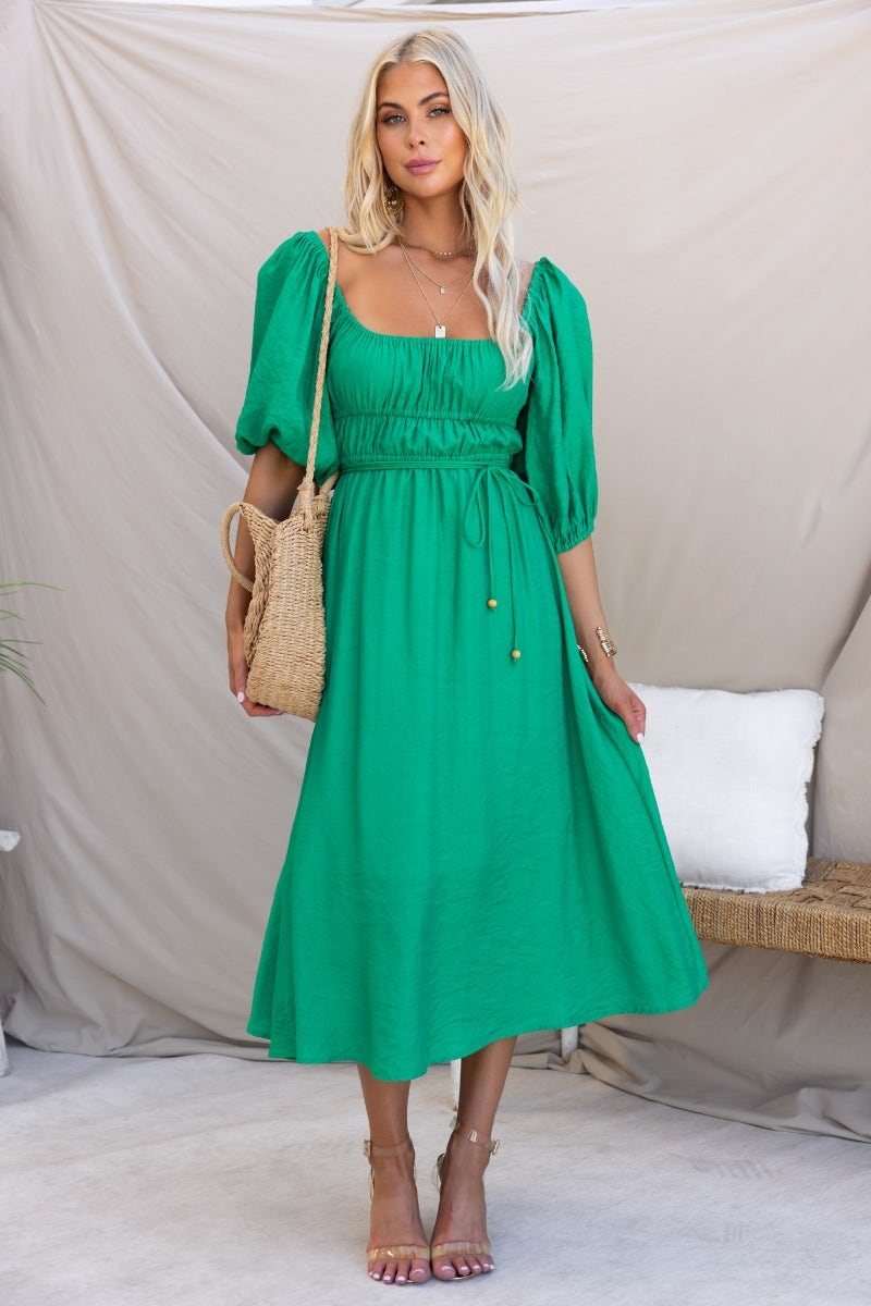 Qove Midi Dress in green with elastic neckline and removable tie, styled with a woven bag and casual sandals.