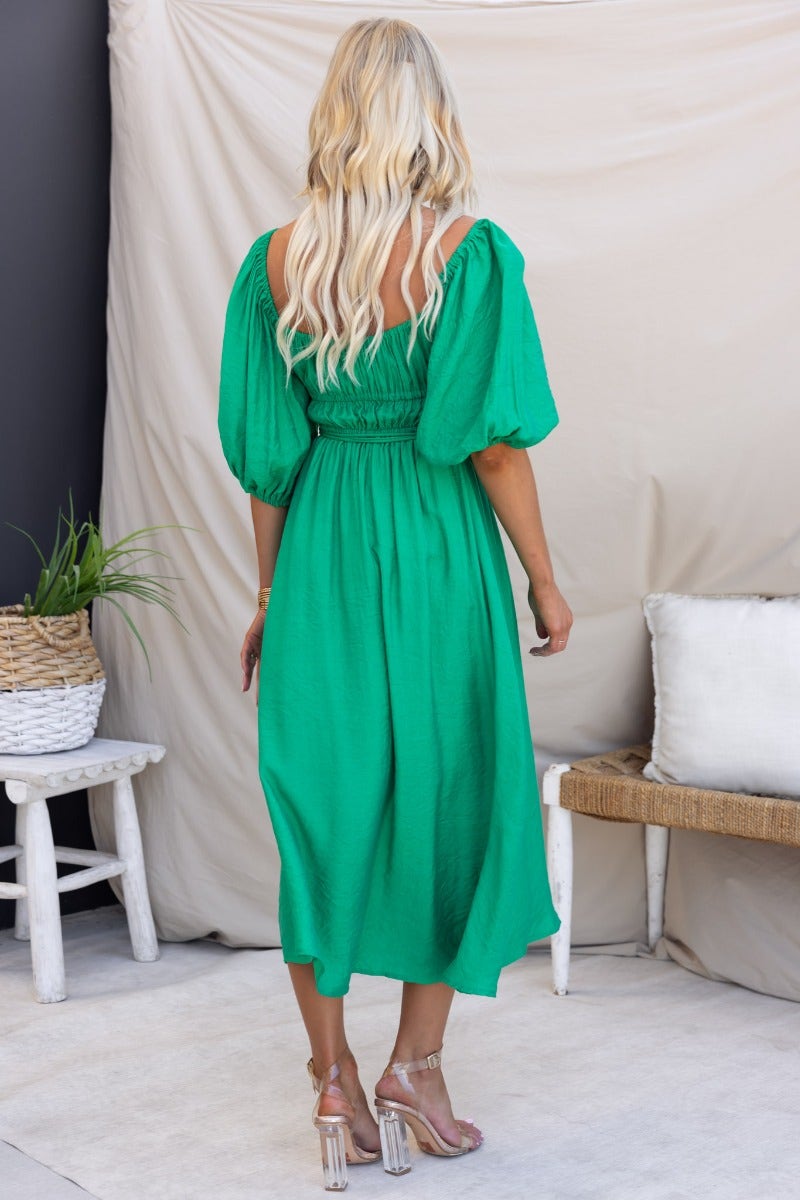Back view of a woman in a green midi dress with elastic neckline, waistband, and puff sleeves.