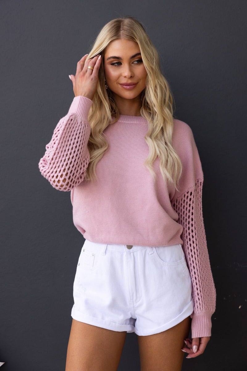 Model wearing a pink Verny Jumper with open weave sleeves styled with white shorts.