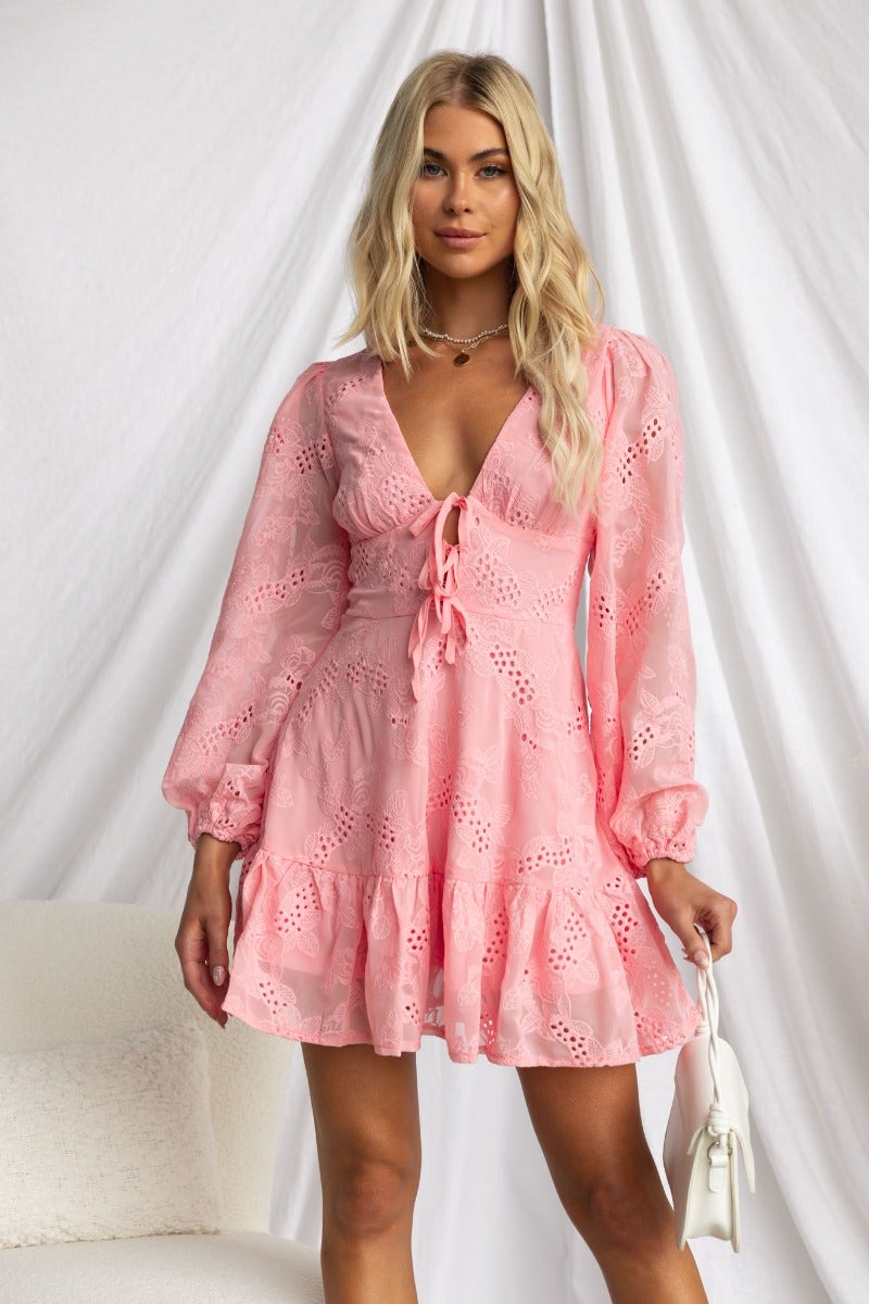 Model wearing Pinolo Dress in pink Anglaise material with V-neckline and tie detail at bust.