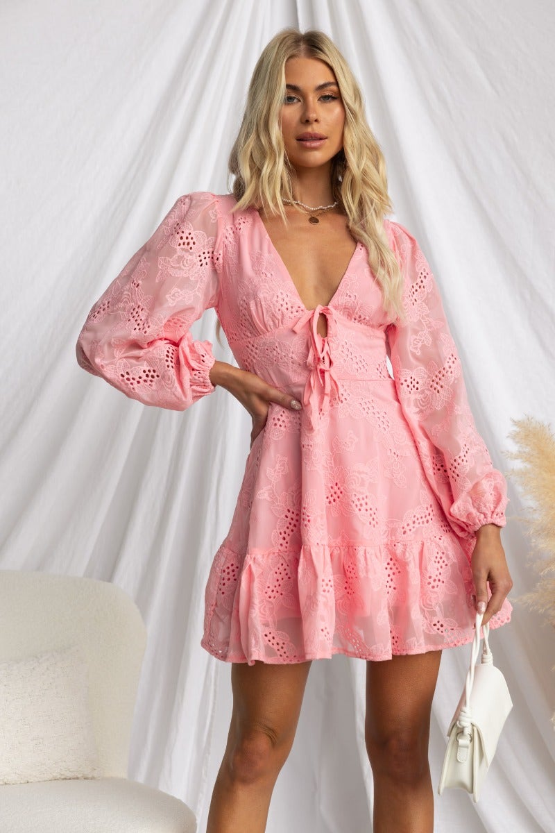 Pinolo Dress in pink Anglaise fabric featuring V-neckline, tie detail, and elastic sleeve cuffs worn by a model.