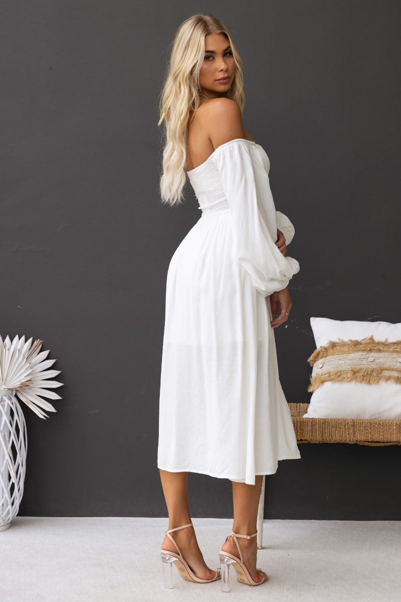 Model wearing a white Lost Love Midi Dress with off-the-shoulder design and pleat detail, styled with clear heels.