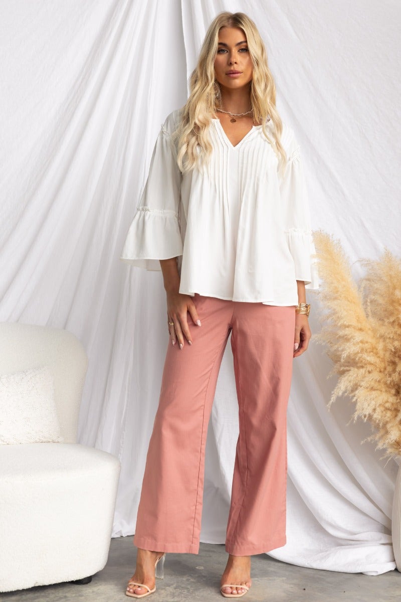 Model wearing a relaxed white cotton blend Cove Top with V-neckline and pleat detail styled with pink pants.