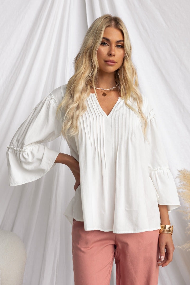 Model wearing a white cotton blend Cove Top with V-neckline and pleat detail, styled with pink trousers.