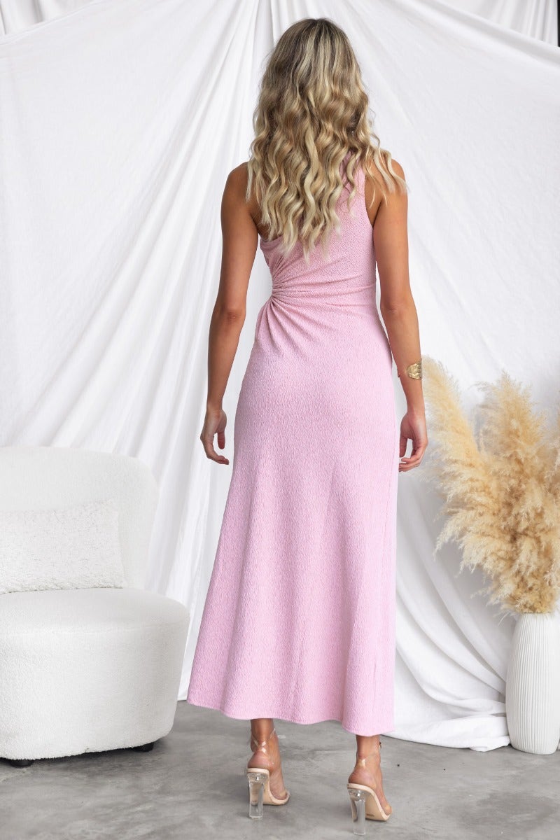 Back view of a woman in a pink Tayan maxi dress with a one-shoulder neckline and adjustable ruching.
