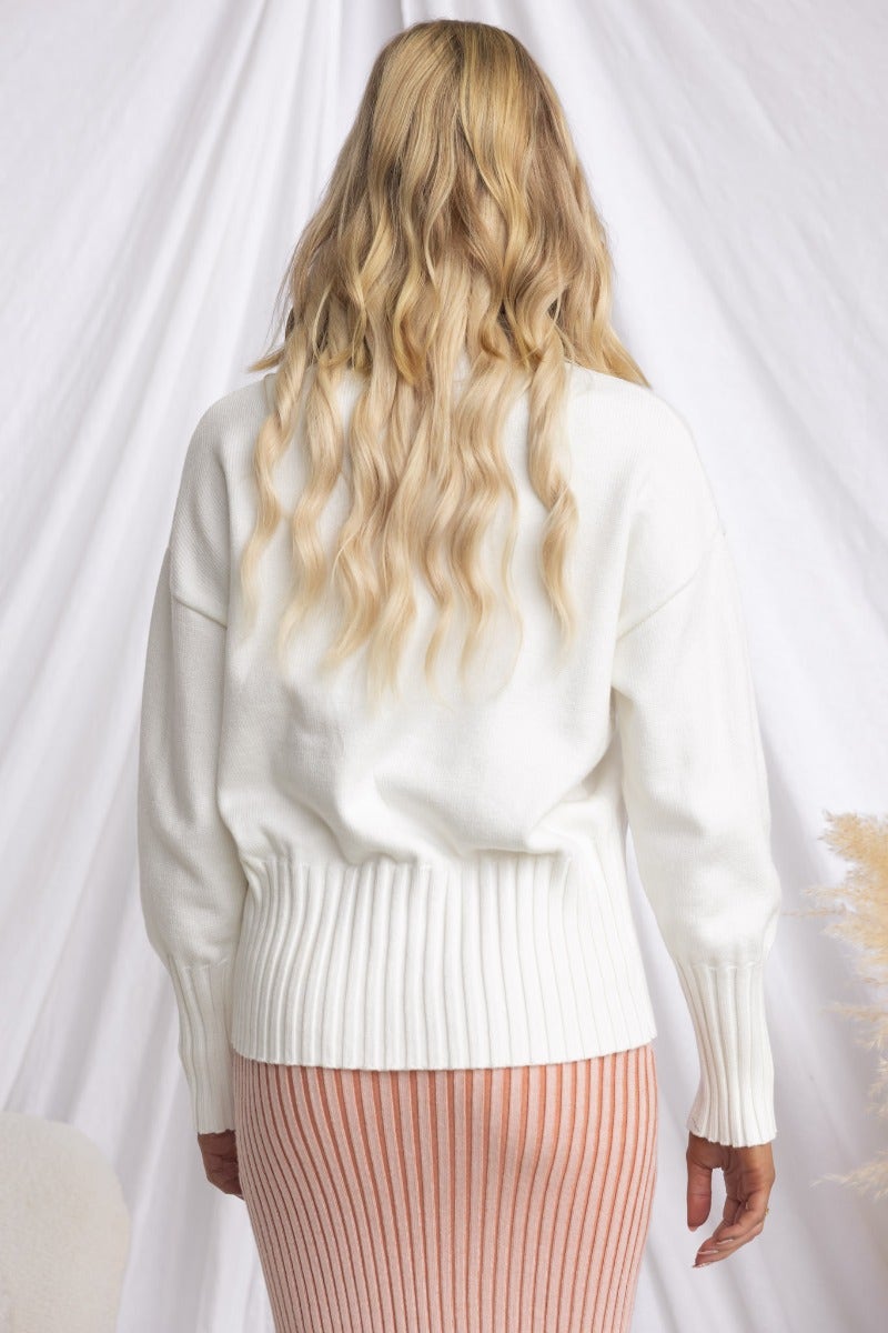 Back view of a woman wearing a white ribbed knit Melika Jumper paired with a striped skirt.