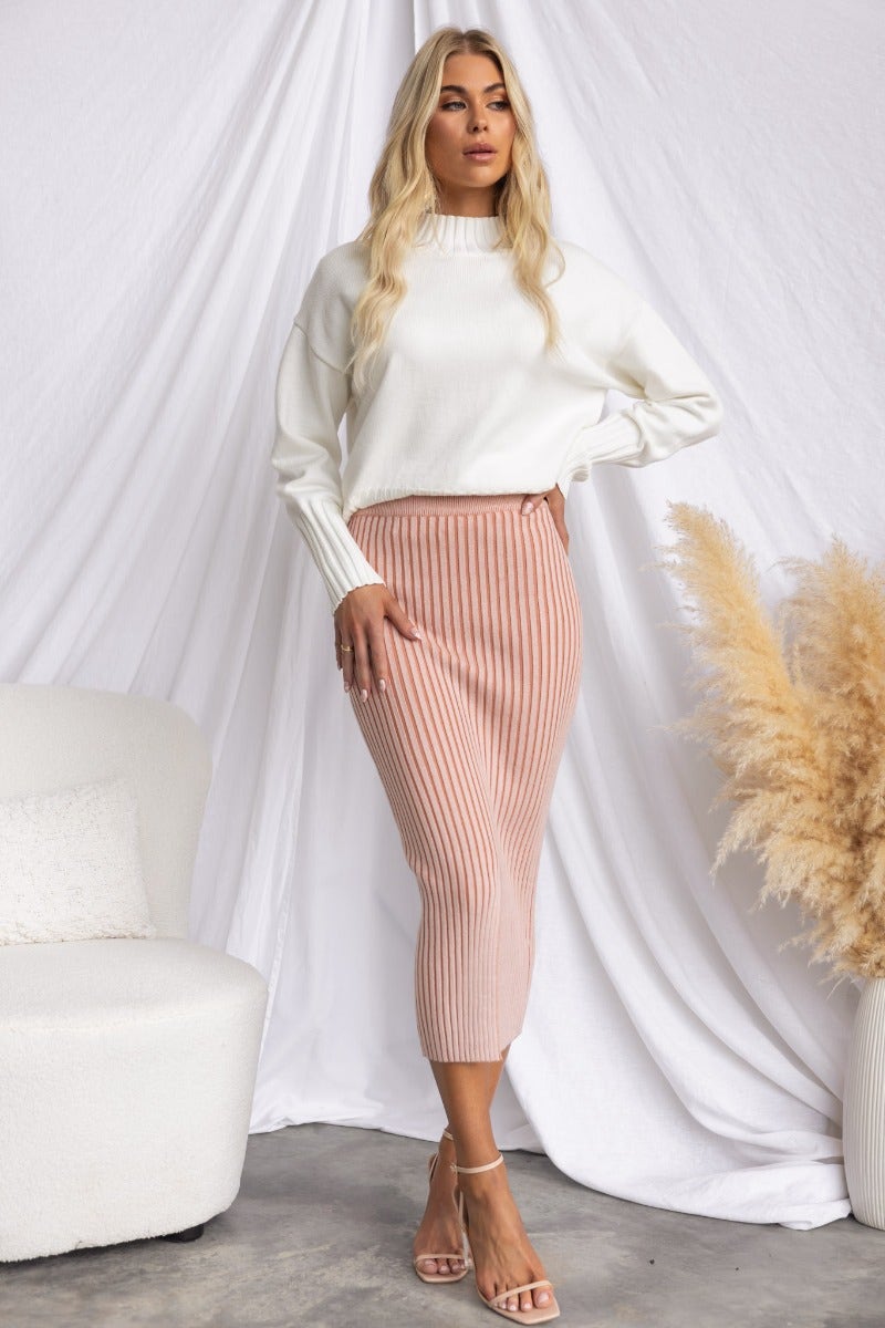Model wearing Melika Jumper with high neckline, styled with a ribbed midi skirt and heels, set against a soft background.