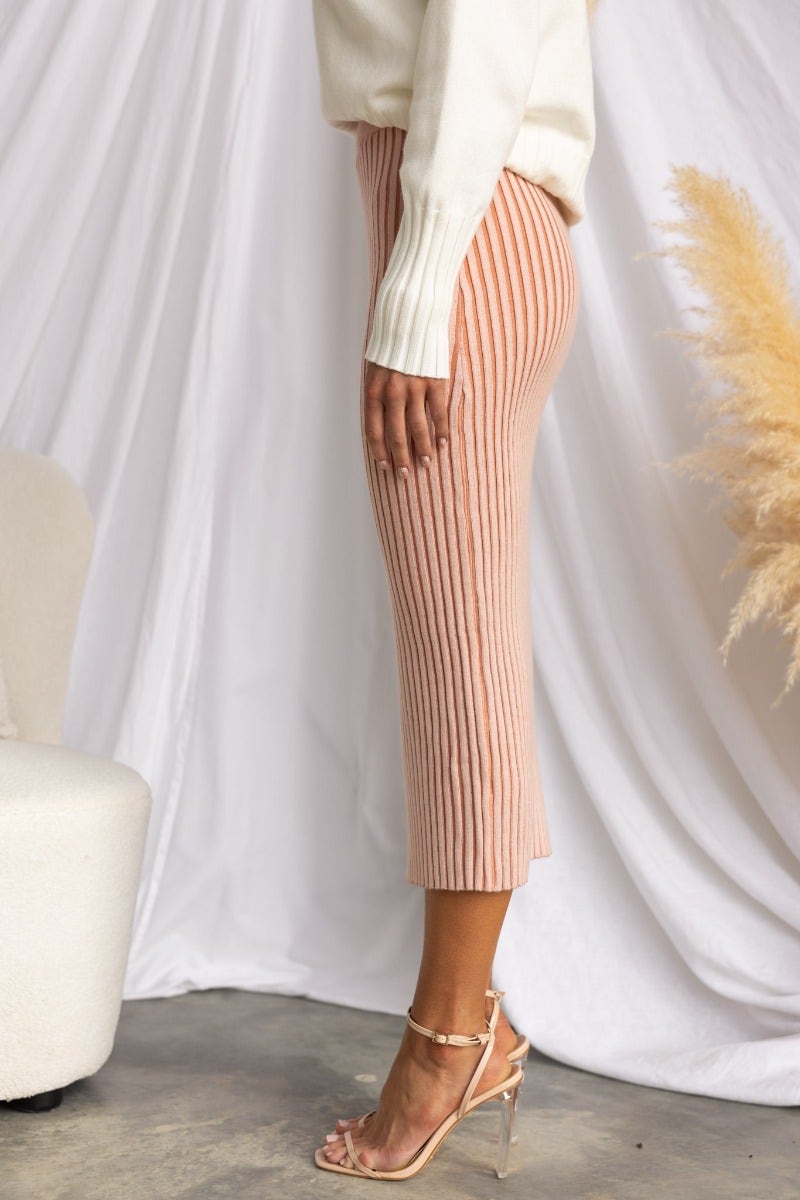 Side view of a ribbed knit midi skirt in pink, featuring an elastic waistband and split front, worn with a light sweater.