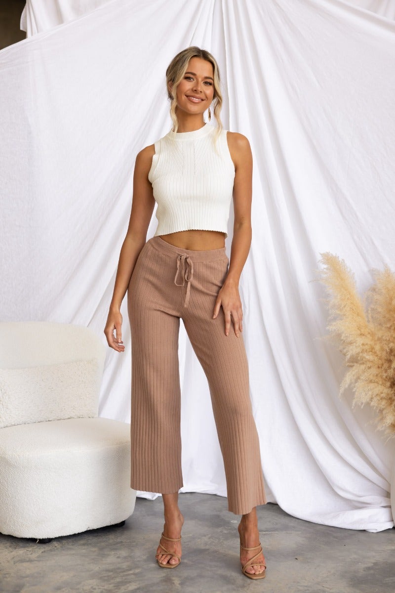 Model wearing Etta Pants, ribbed knit with wide legs and drawstring, styled with a white tank top against a draped backdrop.