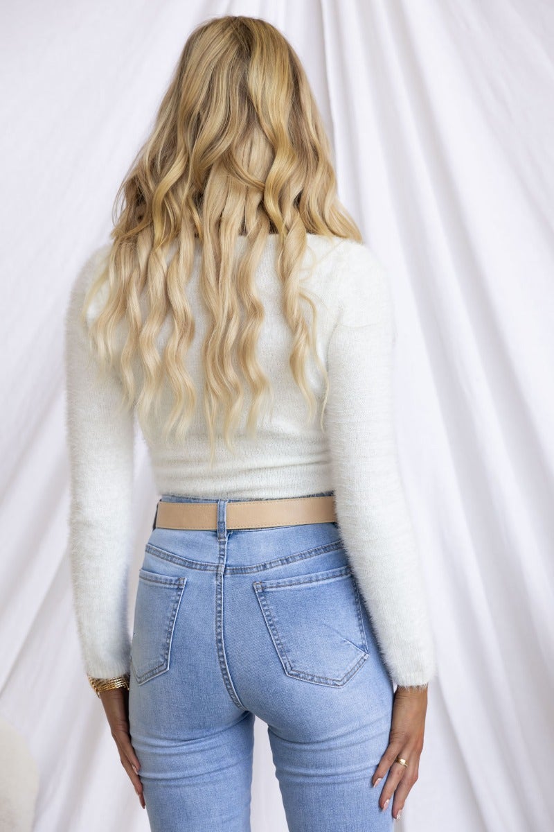 Back view of a model wearing a fluffy white knit bodysuit paired with high-waisted blue jeans.
