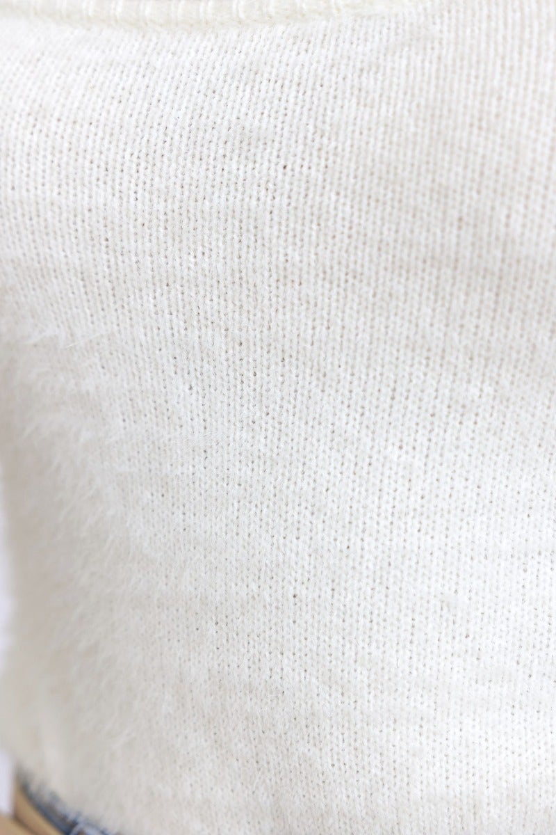 Close-up of a fluffy knit bodysuit fabric in cream color, highlighting the soft texture and fine knit detail.