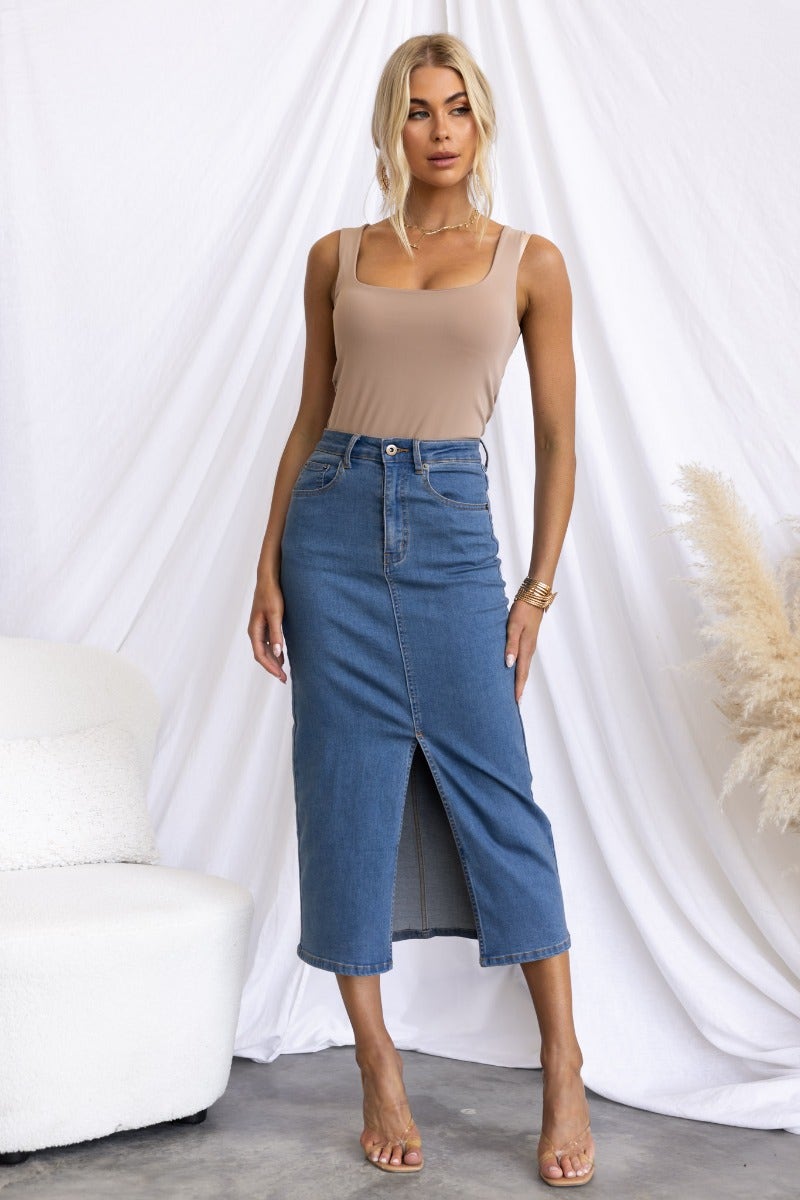 Model wearing Evelyn Denim Midi Skirt, featuring front split and pockets, styled with a beige tank top.