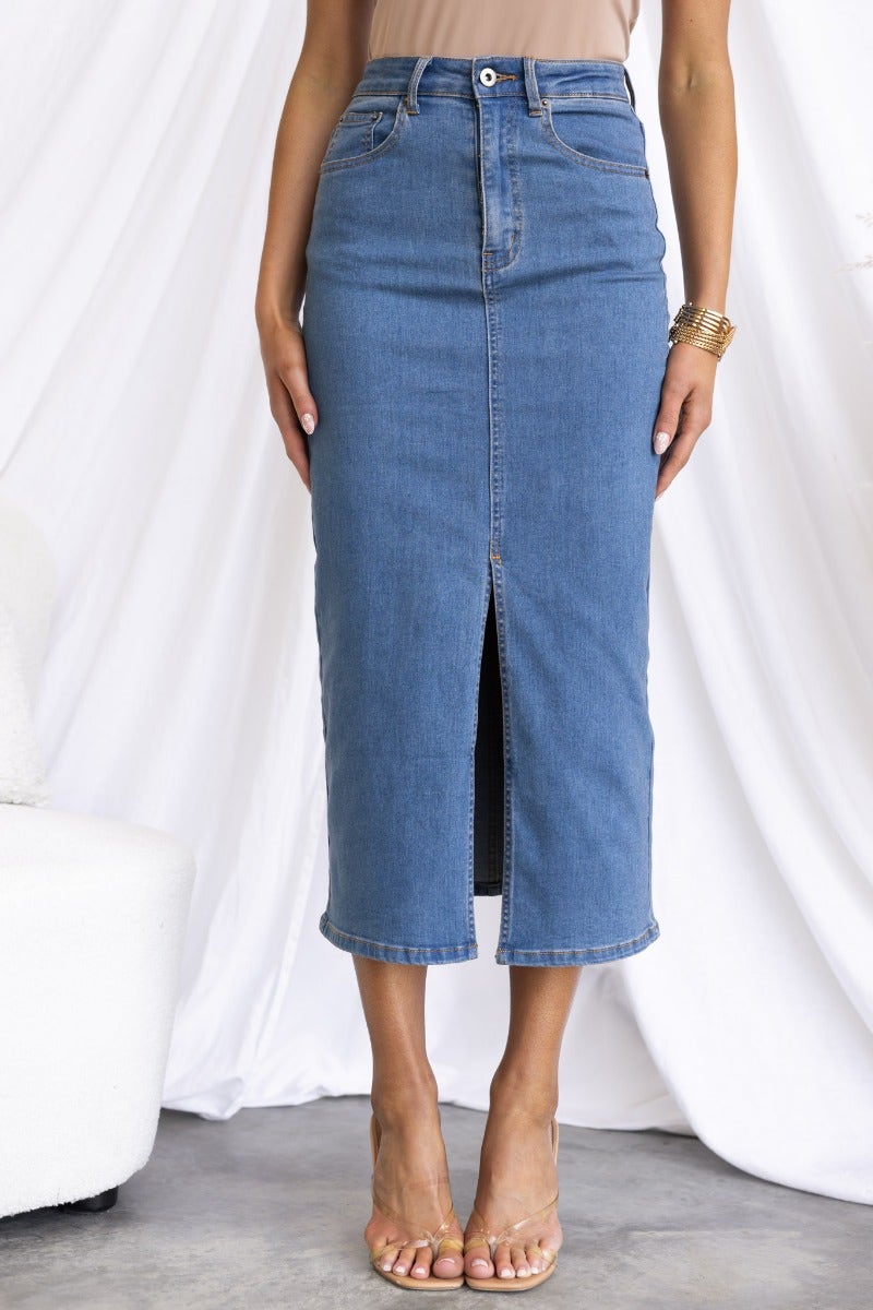 Evelyn Denim Midi Skirt featuring a mid-high waist, front split, and pockets, styled with a nude top and sandals.