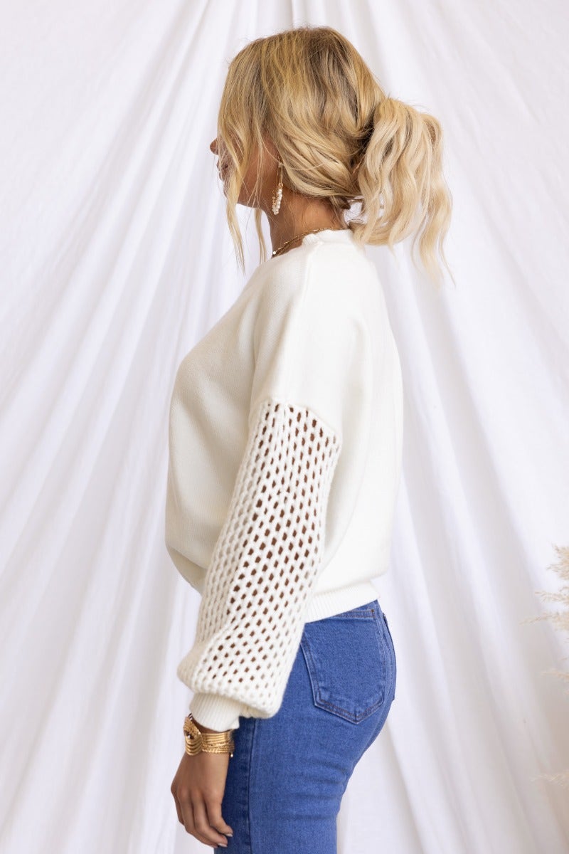 Side view of a woman wearing a white Verny jumper with open weave sleeves styled with blue jeans.