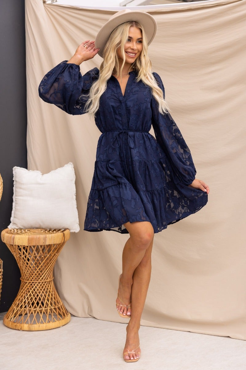 Navy embossed Halston dress with button-up front and elastic sleeves, worn by model in stylish setting.