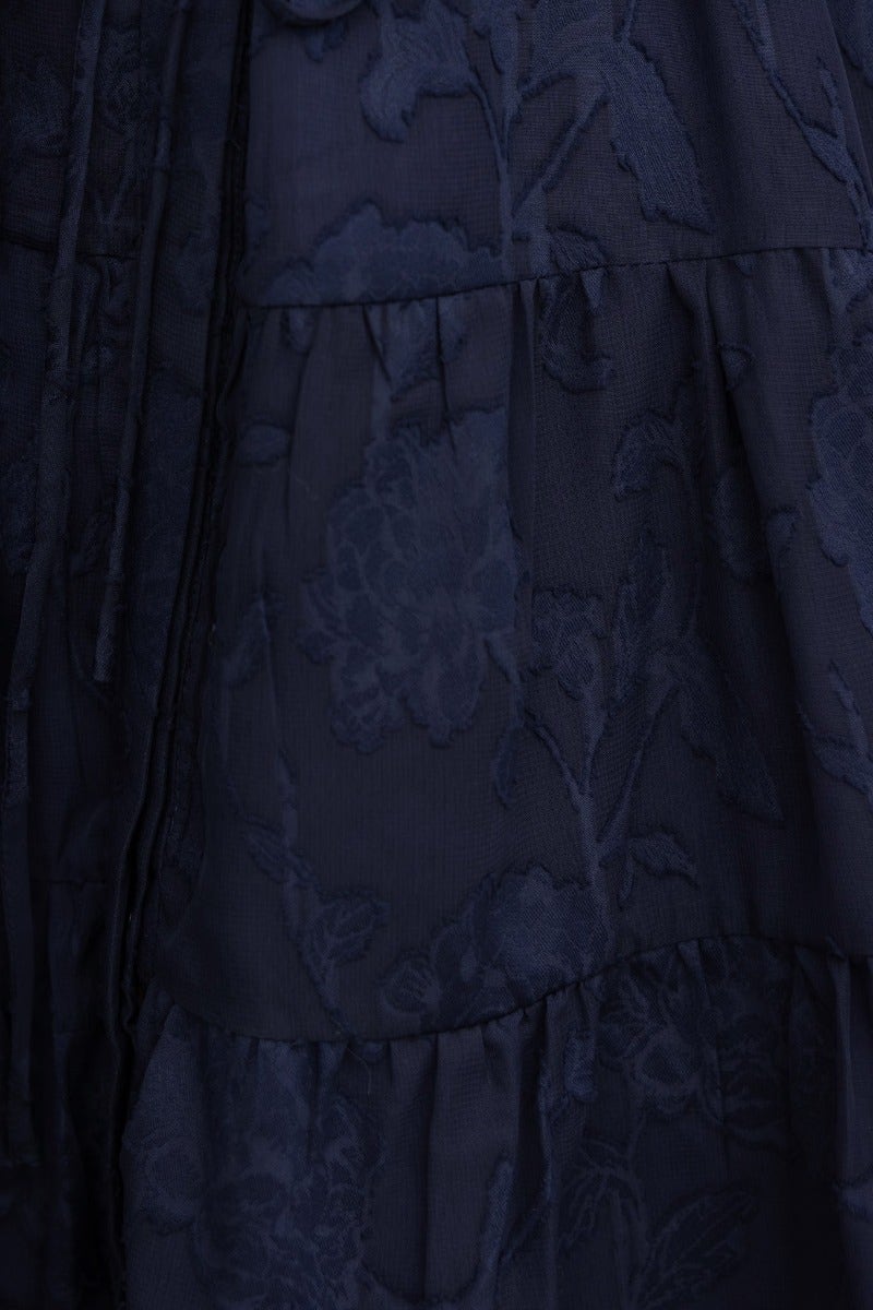 Navy embossed print fabric close-up of Halston dress with floral patterns and tiered design.