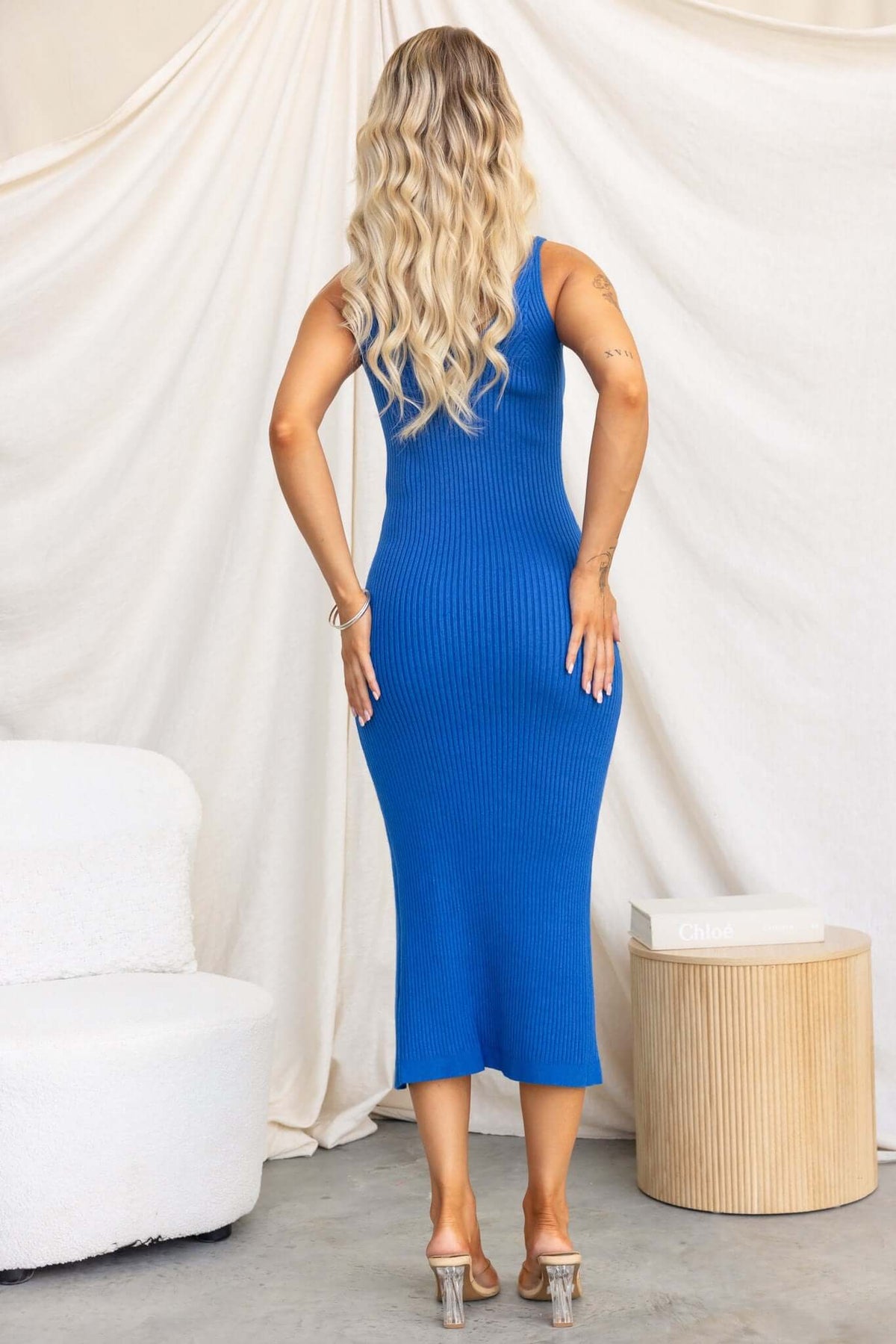 Model showcasing a blue ribbed knit midi dress with a V-neckline and split detail at the back, styled with heels.