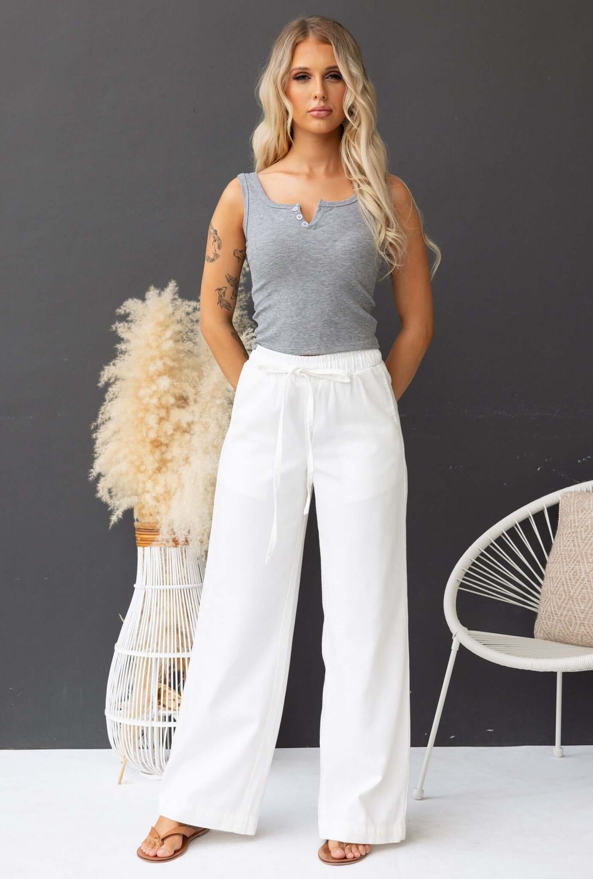 Model showcasing Jordi Top with buttons at bust, paired with white wide-leg pants in a stylish indoor setting.