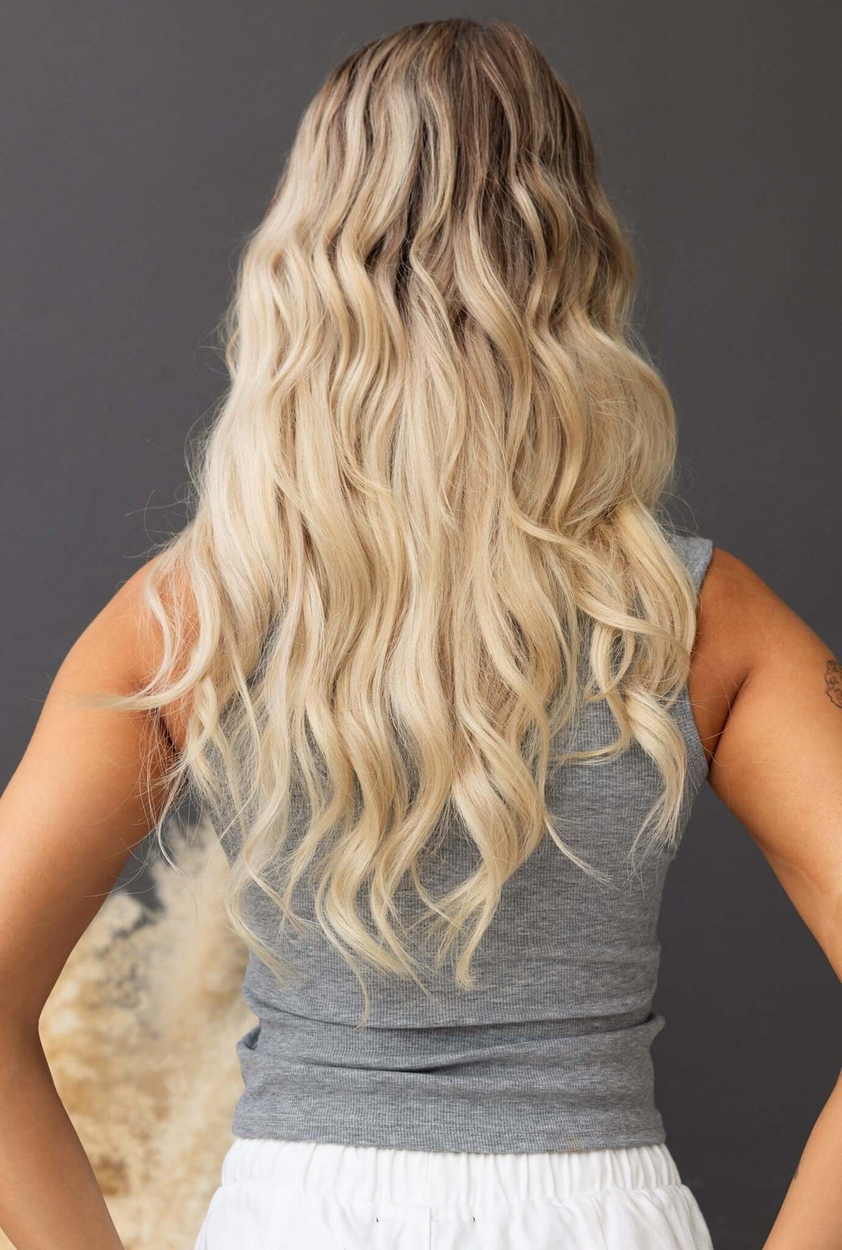 Back view of a woman with long wavy blonde hair wearing a gray sleeveless top.