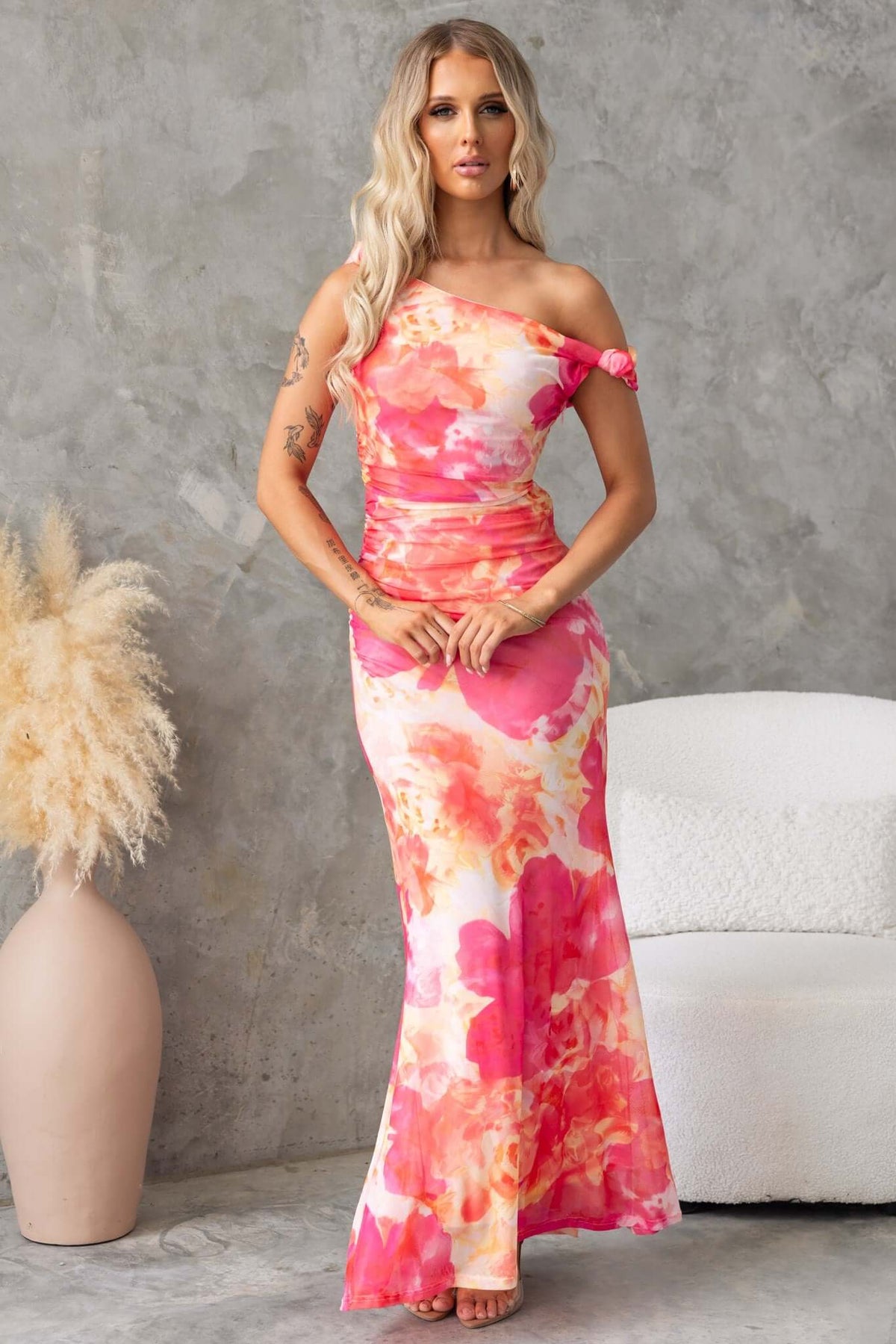 Woman in Fellaire Maxi Dress with asymmetric neckline and floral design, showcasing stylish knots at the strap.