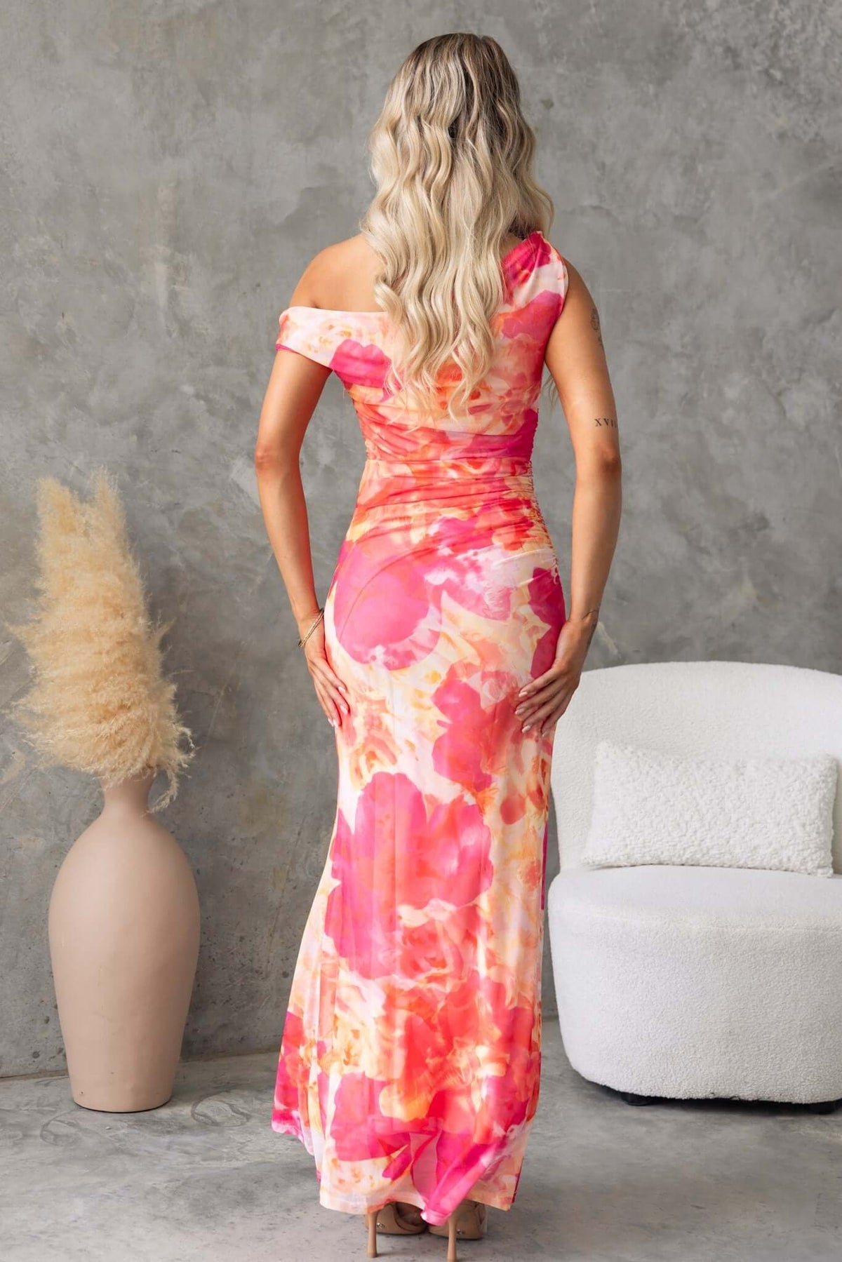 Back view of a woman in a Fellaire maxi dress with floral print, showcasing an asymmetric neckline and strap knots.