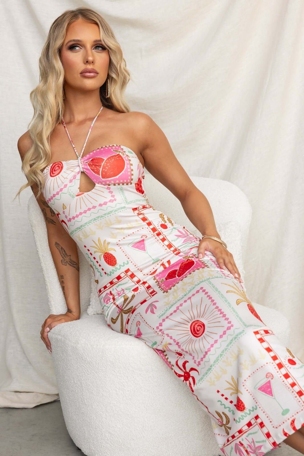 Model wearing Carianne Midi Dress, a colorful strapless dress with a keyhole detail, sitting gracefully in a stylish pose.