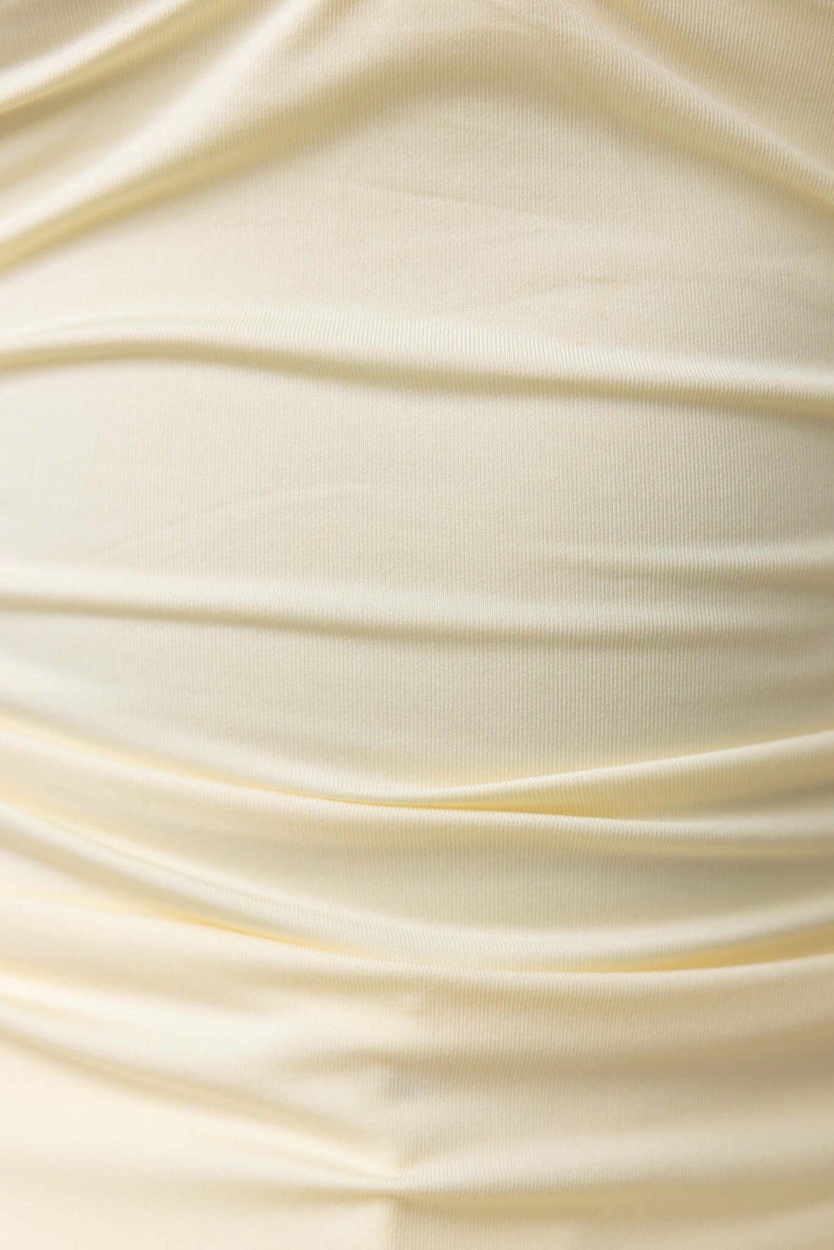 Close-up of soft, stretched fabric in cream color showcasing delicate ruching texture.