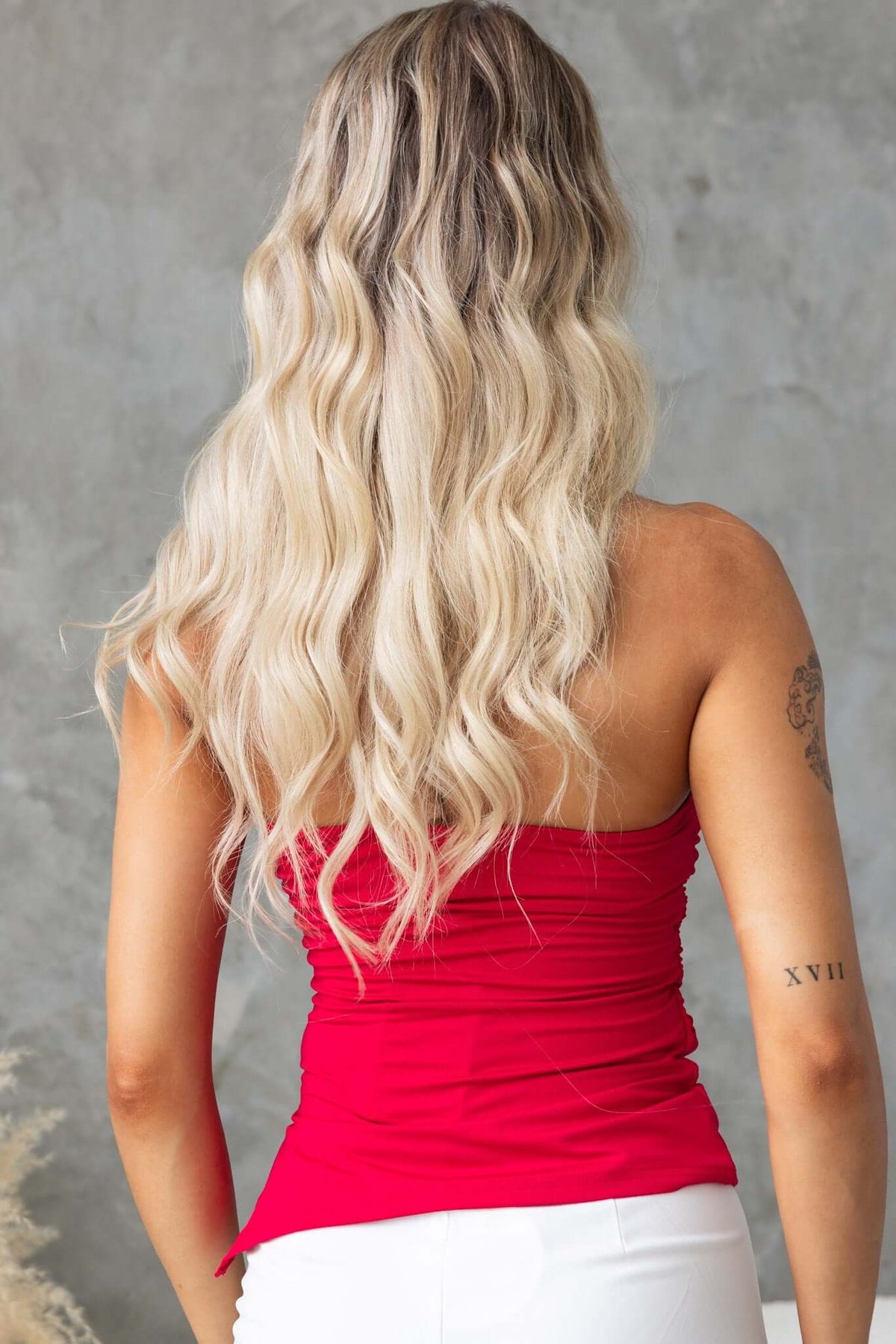 Back view of a model wearing a red strapless Kylie Top with ruched detailing and loose, wavy blonde hair.