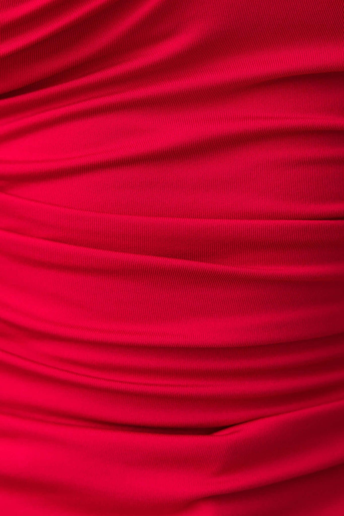 Close-up of textured red fabric with elegant ruching detail, showcasing a smooth and stretchy material perfect for stylish tops.