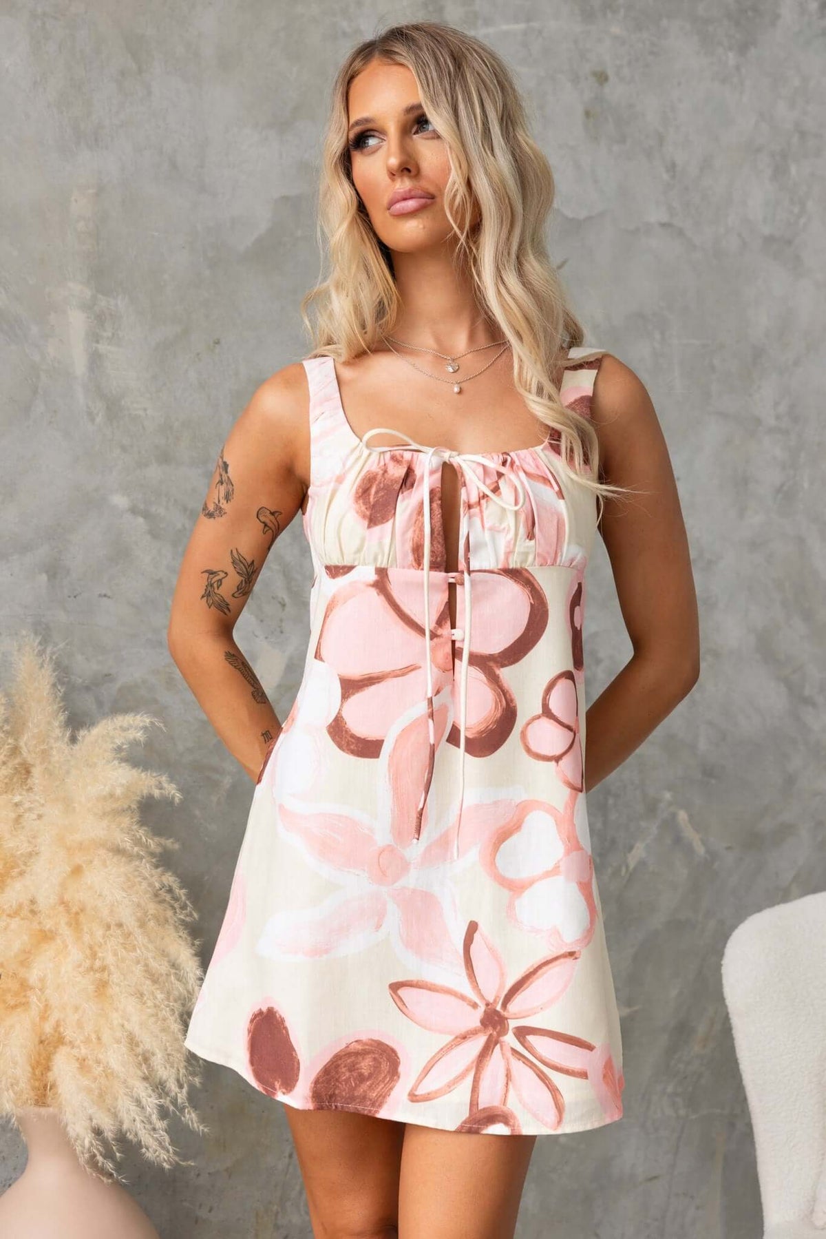 Model wearing Hathaway Dress with floral print, featuring tie at bust and button-up front, showcased in a stylish setting.