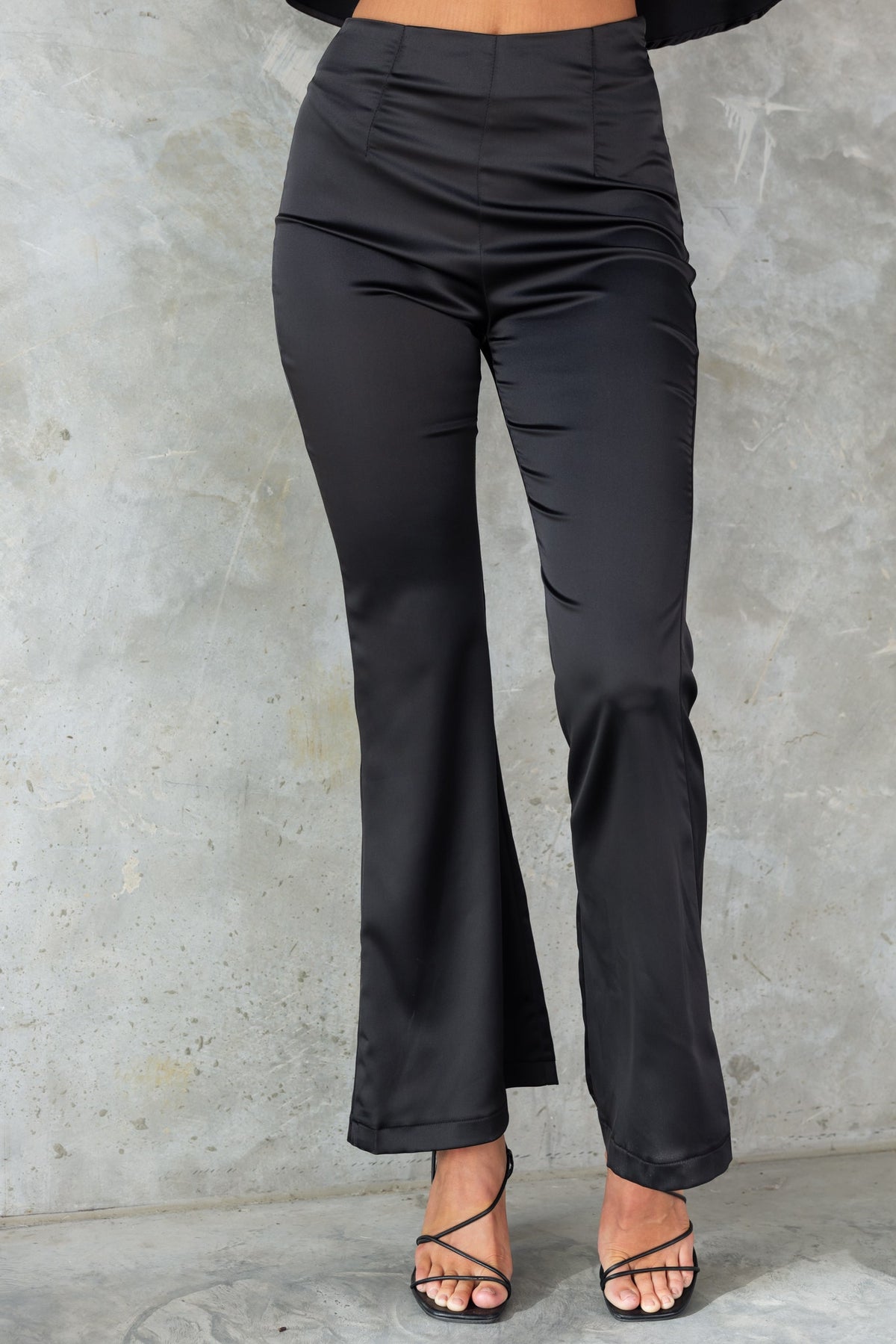 Black Amore Pants with mid-high waist and flare leg design, featuring a sleek satin look and firm stretch fit.