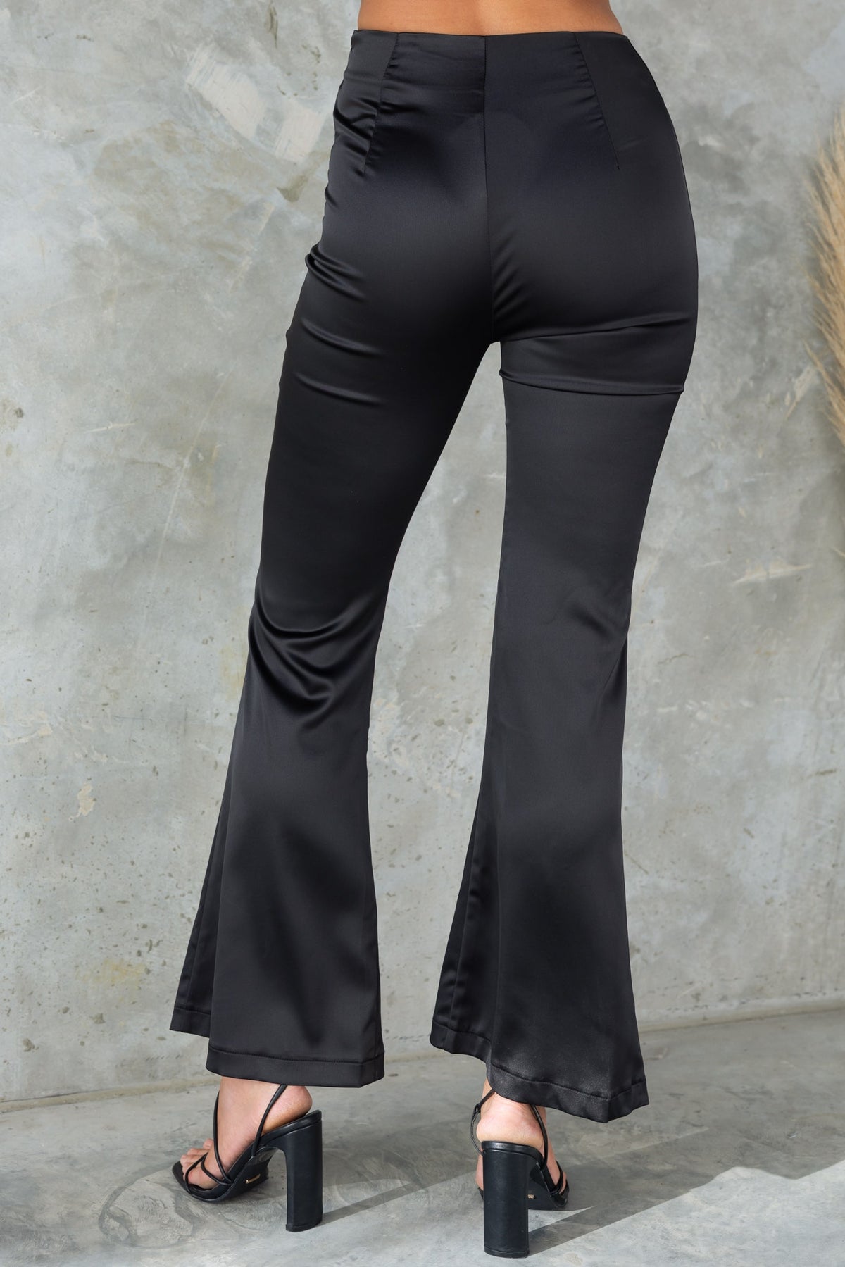 Back view of Amore Pants in black, featuring mid-high waist, flare leg, and a sleek satin look.