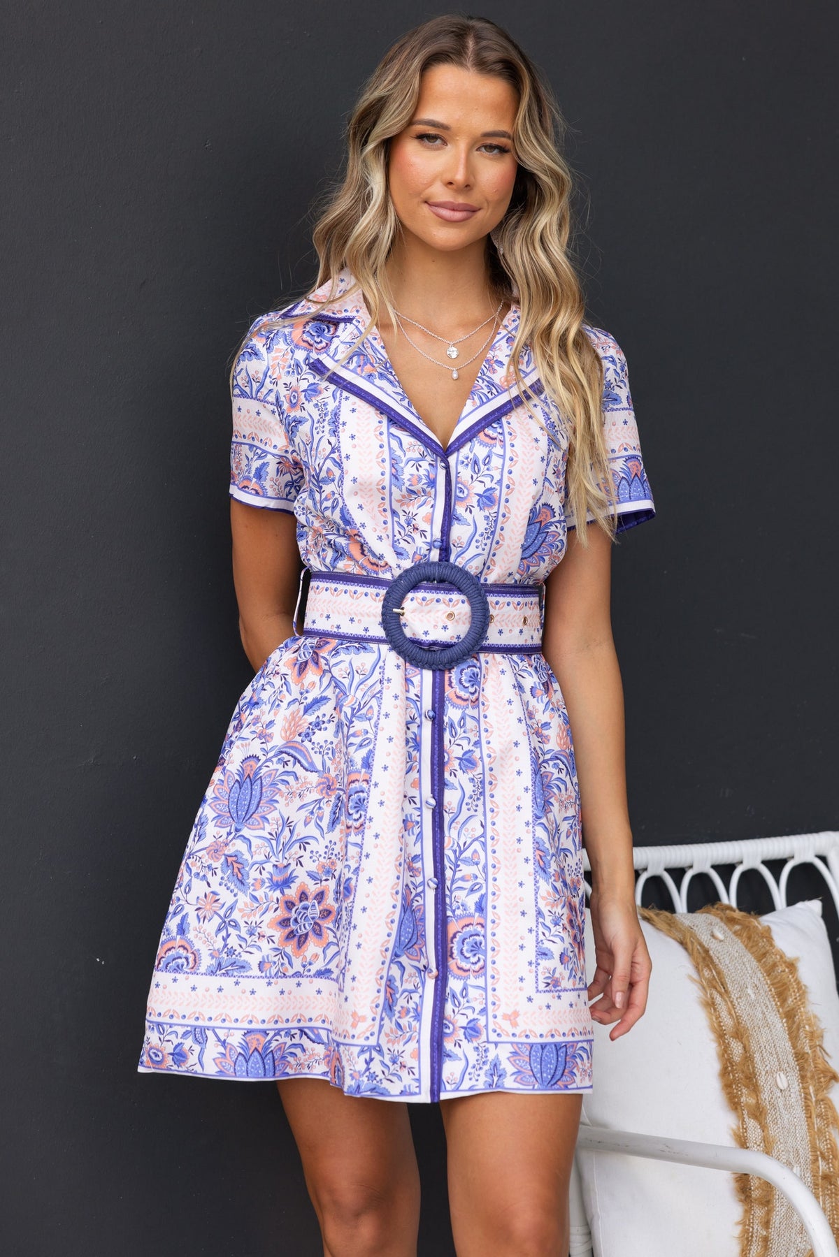 Model wearing the Navine Dress, a short button-up dress with a removable belt and floral pattern.