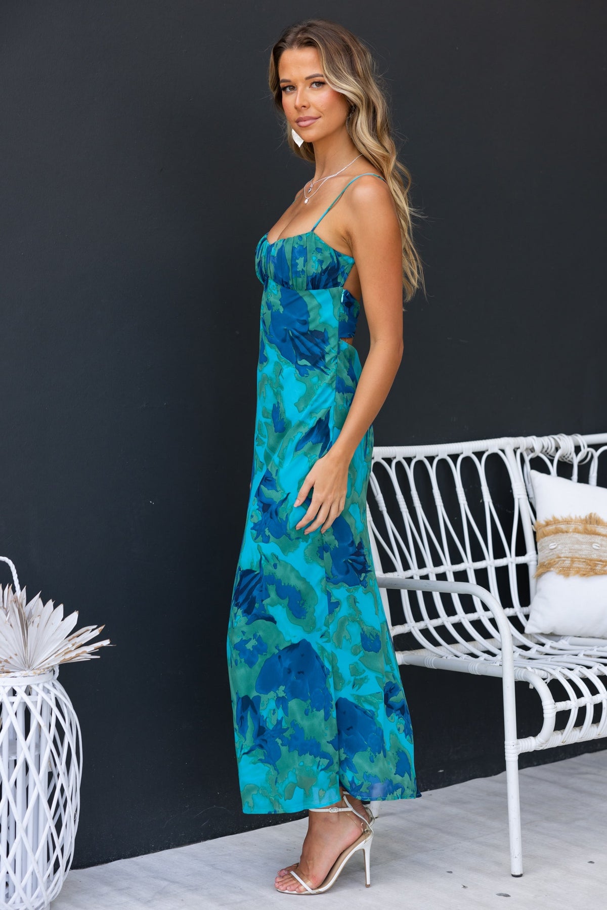 Freyda Maxi Dress in vibrant floral print, featuring adjustable straps and a cut-out back, styled with heels.
