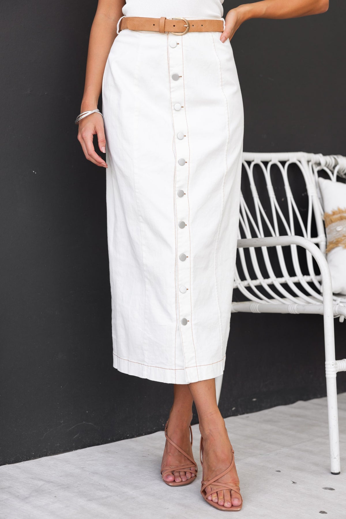 White denim midi skirt with button-up front and tan belt, styled for a chic look.