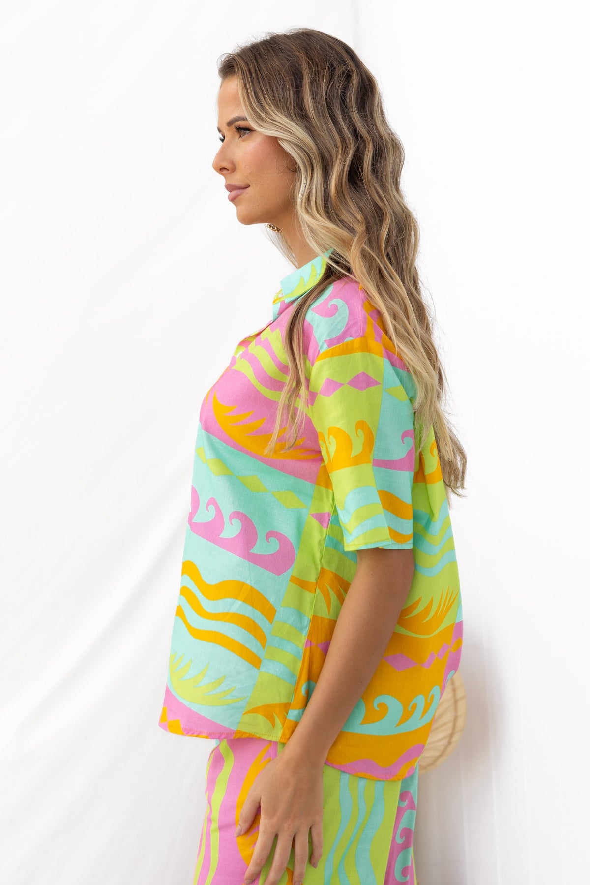Profile view of a woman wearing a colorful Verney Shirt with wave patterns in pink, blue, and yellow.