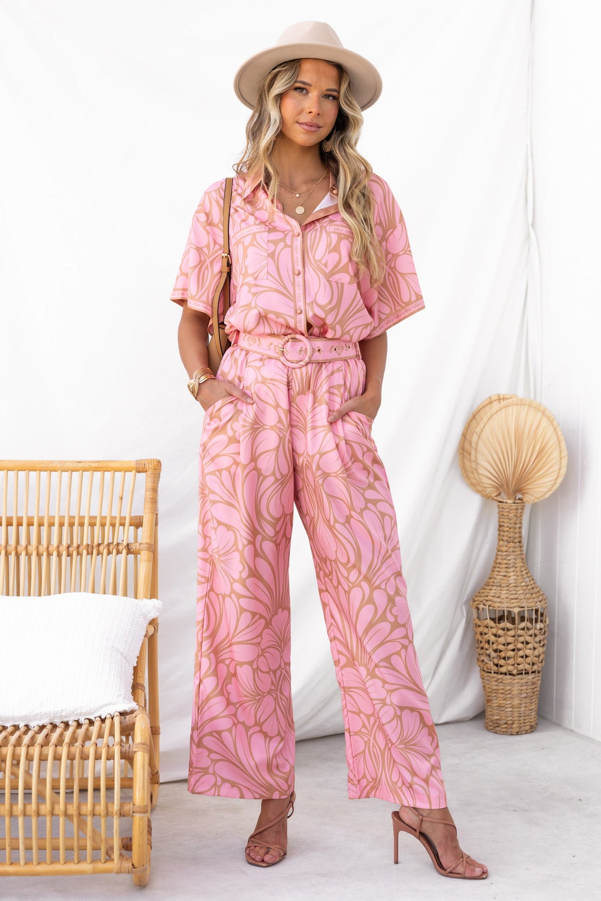 Woman in pink Raddix Pants with floral pattern, mid-high waist, and removable belt, styled with a hat.