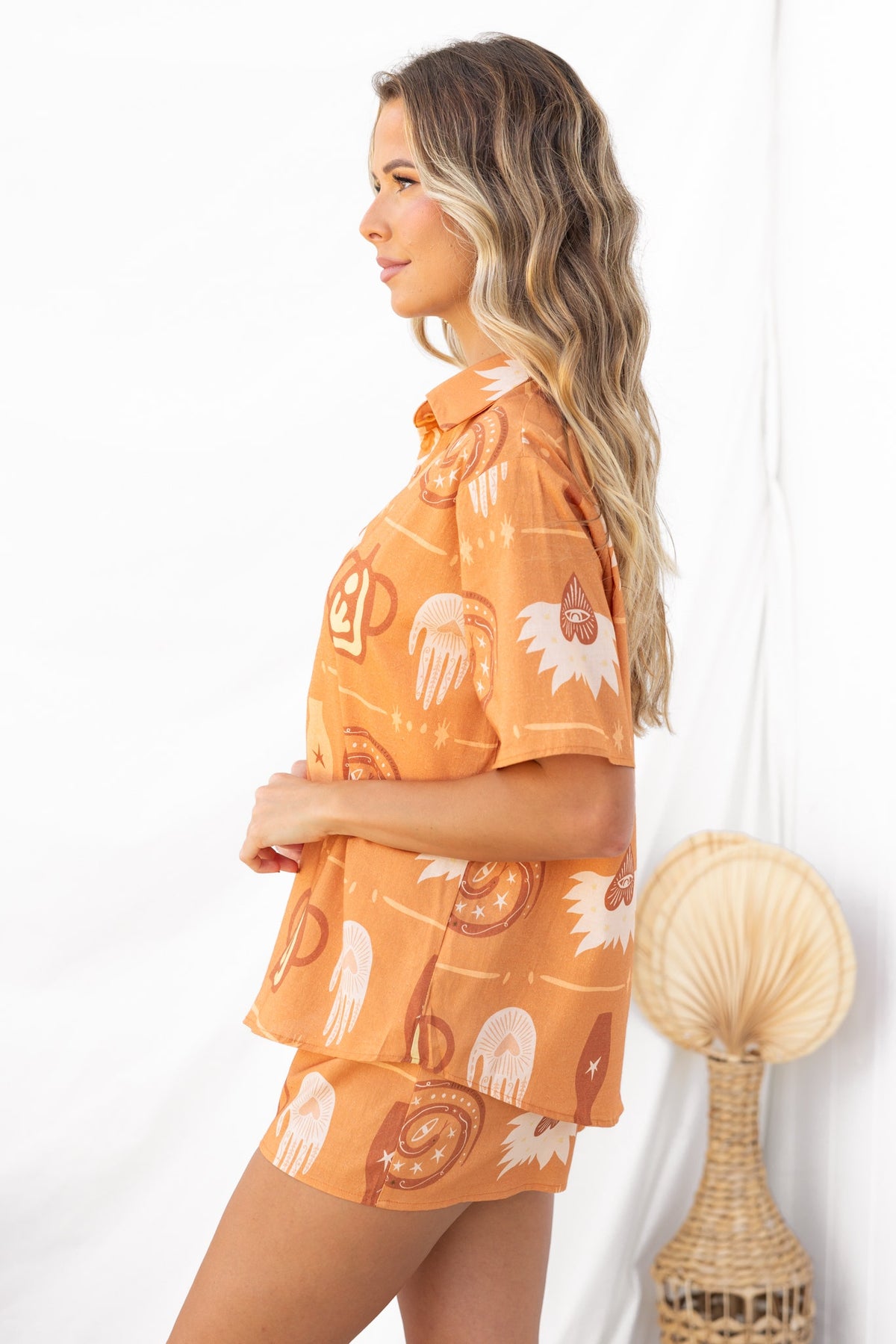 Model wearing Koffie Set, featuring a button-up shirt and shorts with a fun print in warm orange tones.