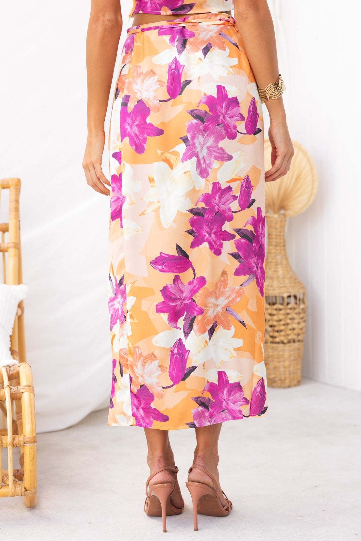 Back view of a model wearing a floral print Nerida Wrap Midi Skirt with an asymmetric hem and satin finish.